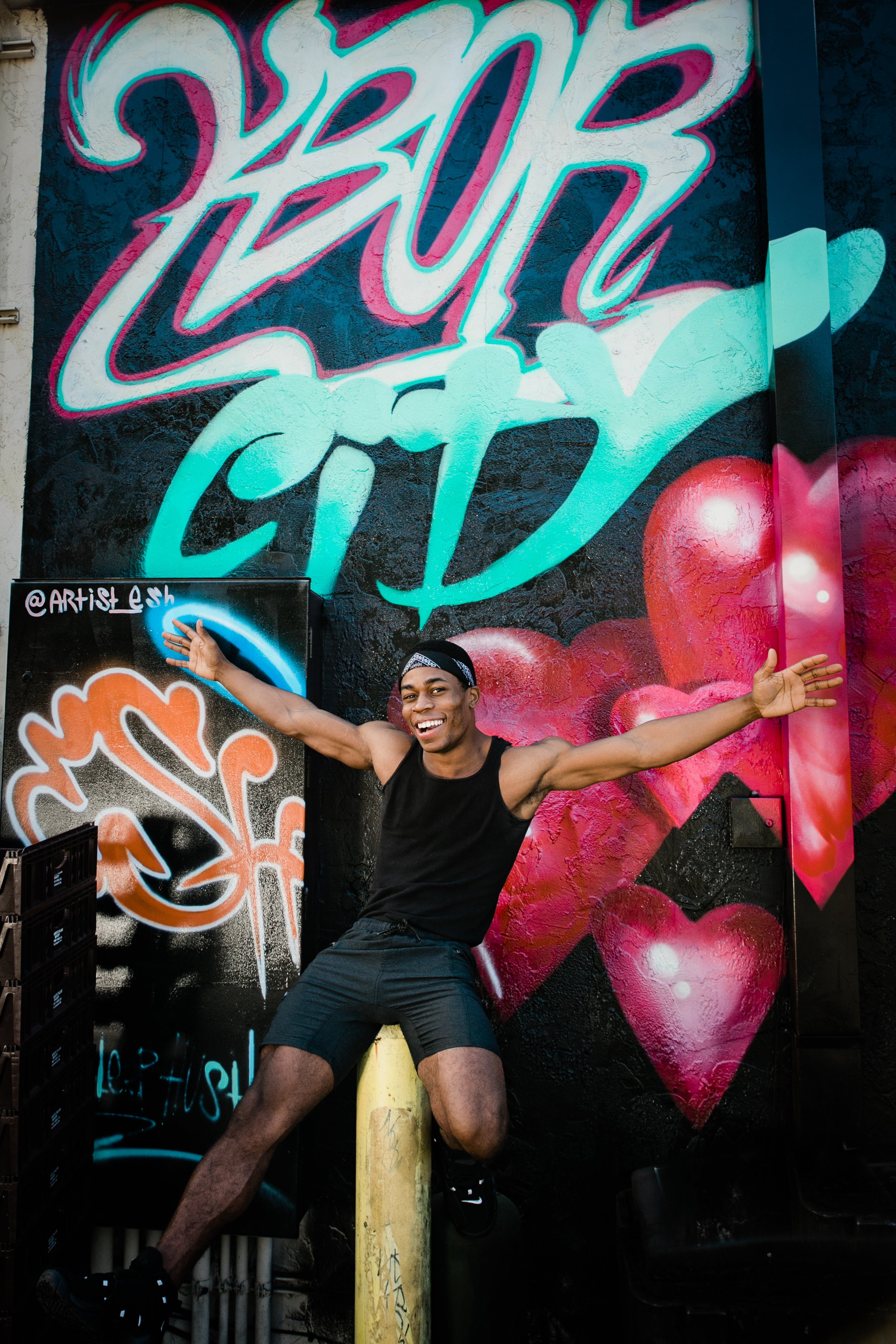 Colorful Ybor City mural in the background with man balancing on a yellow pole in foreground, arms outstretched