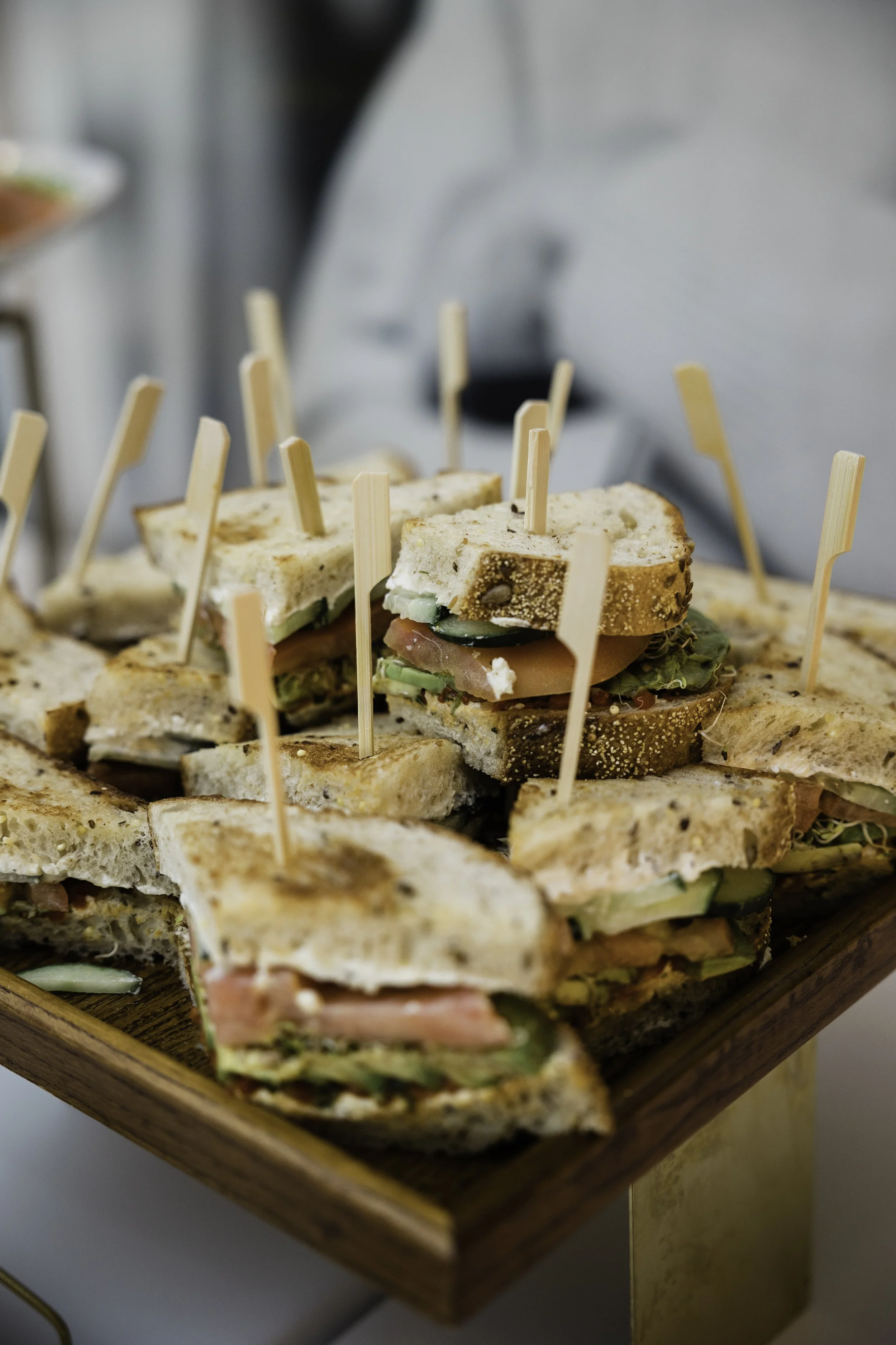 Close-up of assorted sandwiches with various fillings, topped with wooden toothpick skewers, arranged on a wooden platter.
