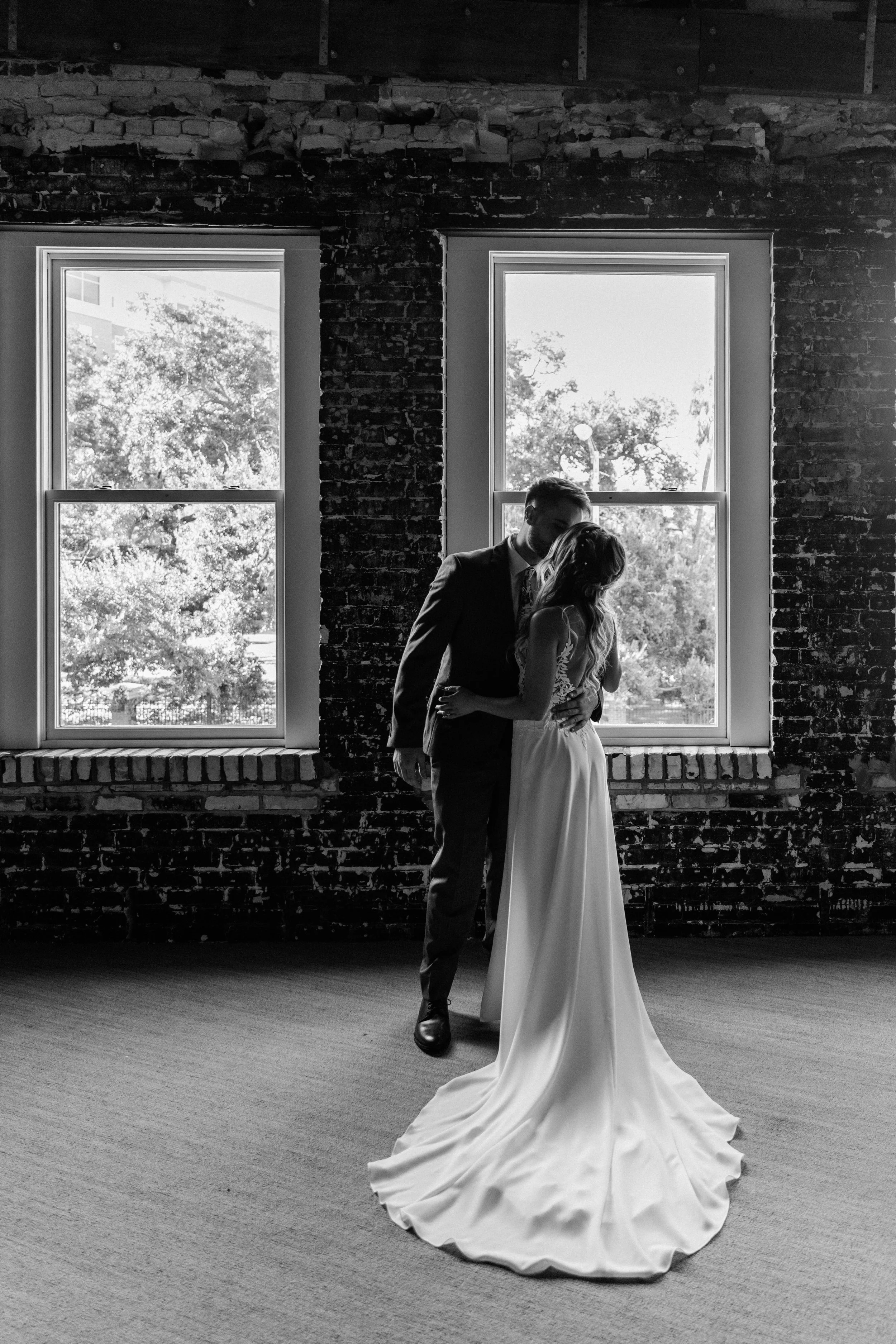 Black and white image of a bride and groom kissing in front of a brick wall and windows at Oxford Exchange.