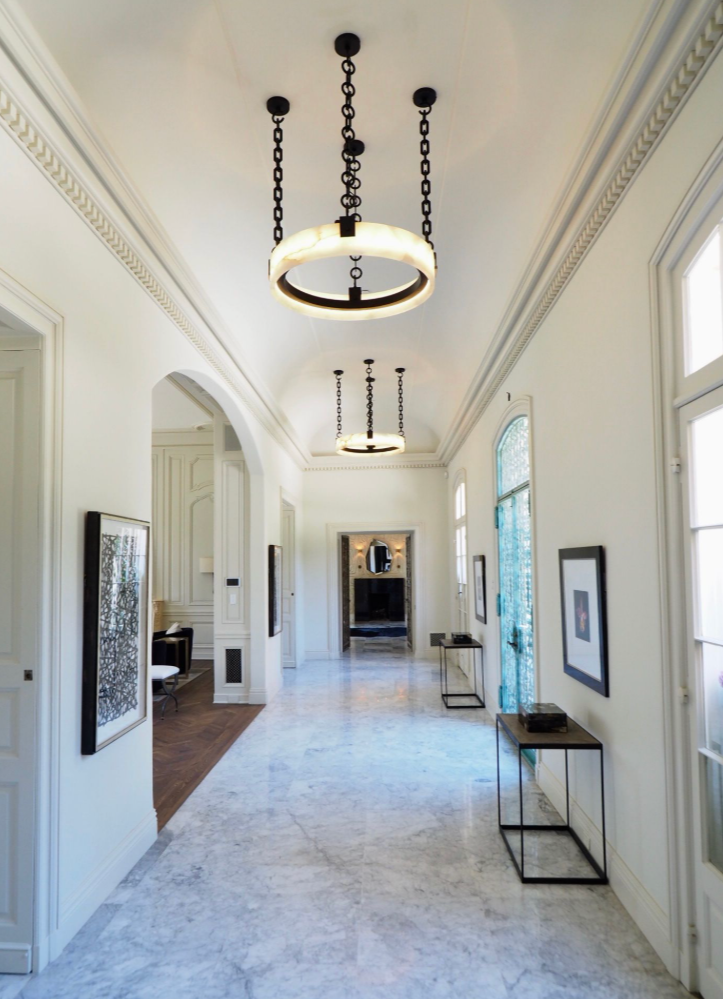 Elegant hallway with white walls, marble flooring, large arched windows, and modern circular chandeliers.