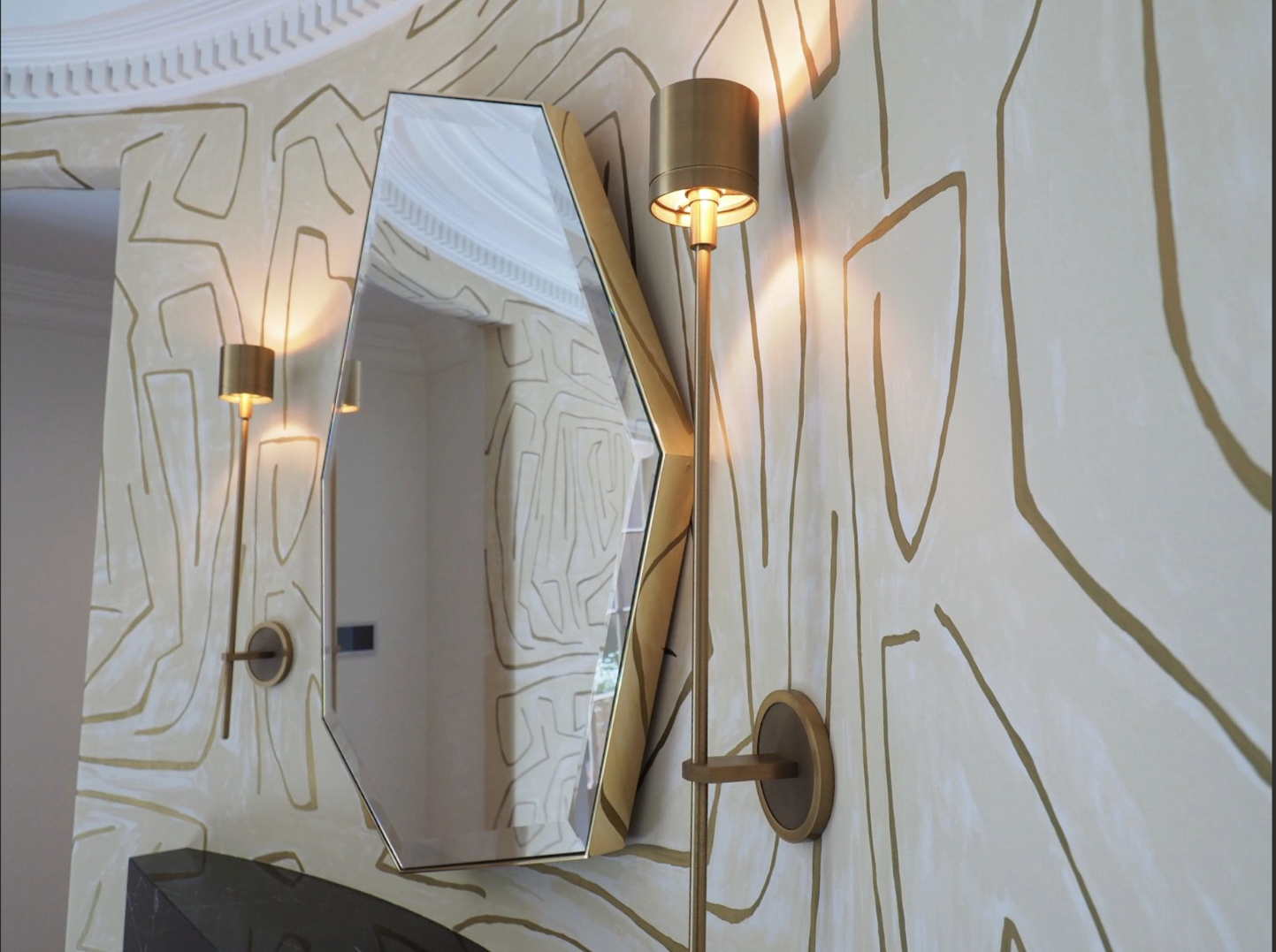 Decorative hallway with a large mirror, modern wall sconces, and gold patterned wallpaper.