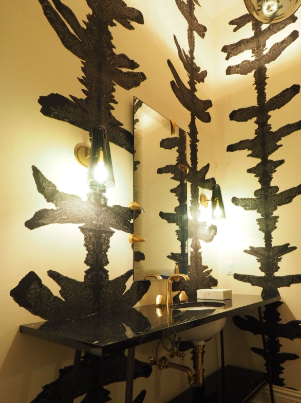 Decorative bathroom with black abstract patterns on the walls and ceiling, gold fixtures, a rectangular mirror, and pendant lights.