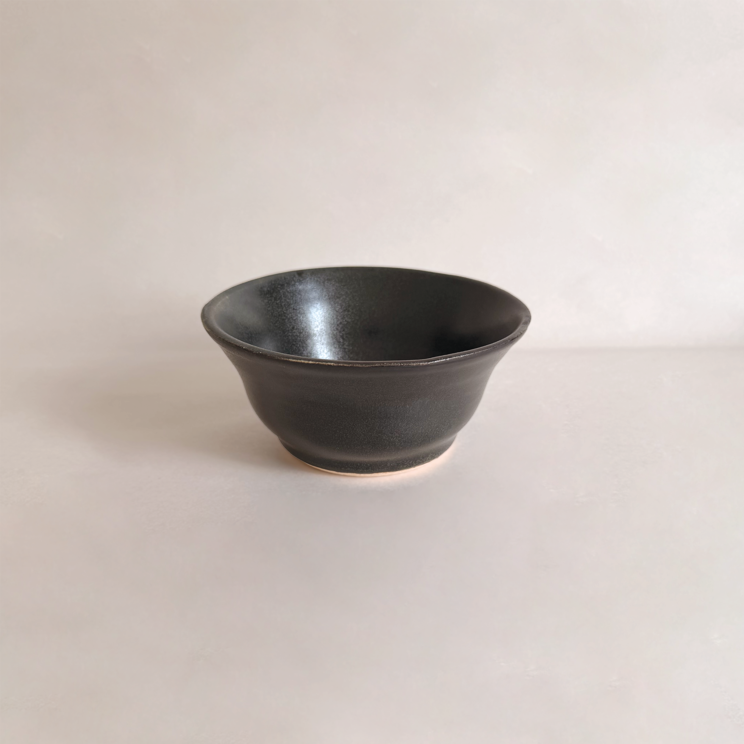 Black ceramic bowl on a white surface with a plain white background.