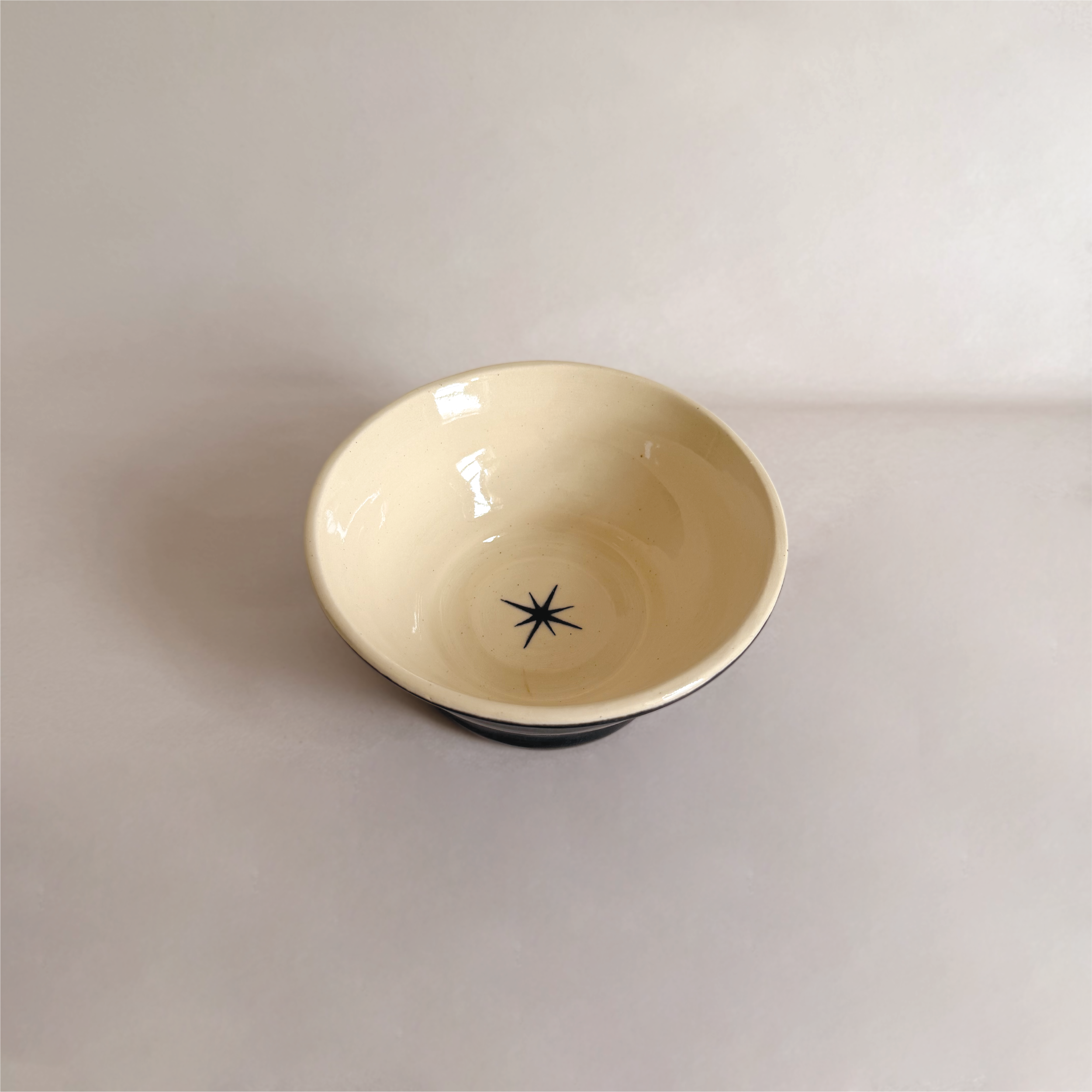 Top view of a ceramic mug with cream interior and a black starburst design at the bottom on a white surface.