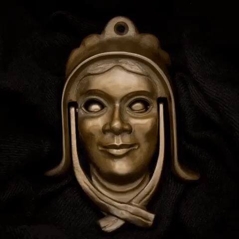 A metal pendant depicting a smiling woman's face with long hair, set against a dark fabric background.