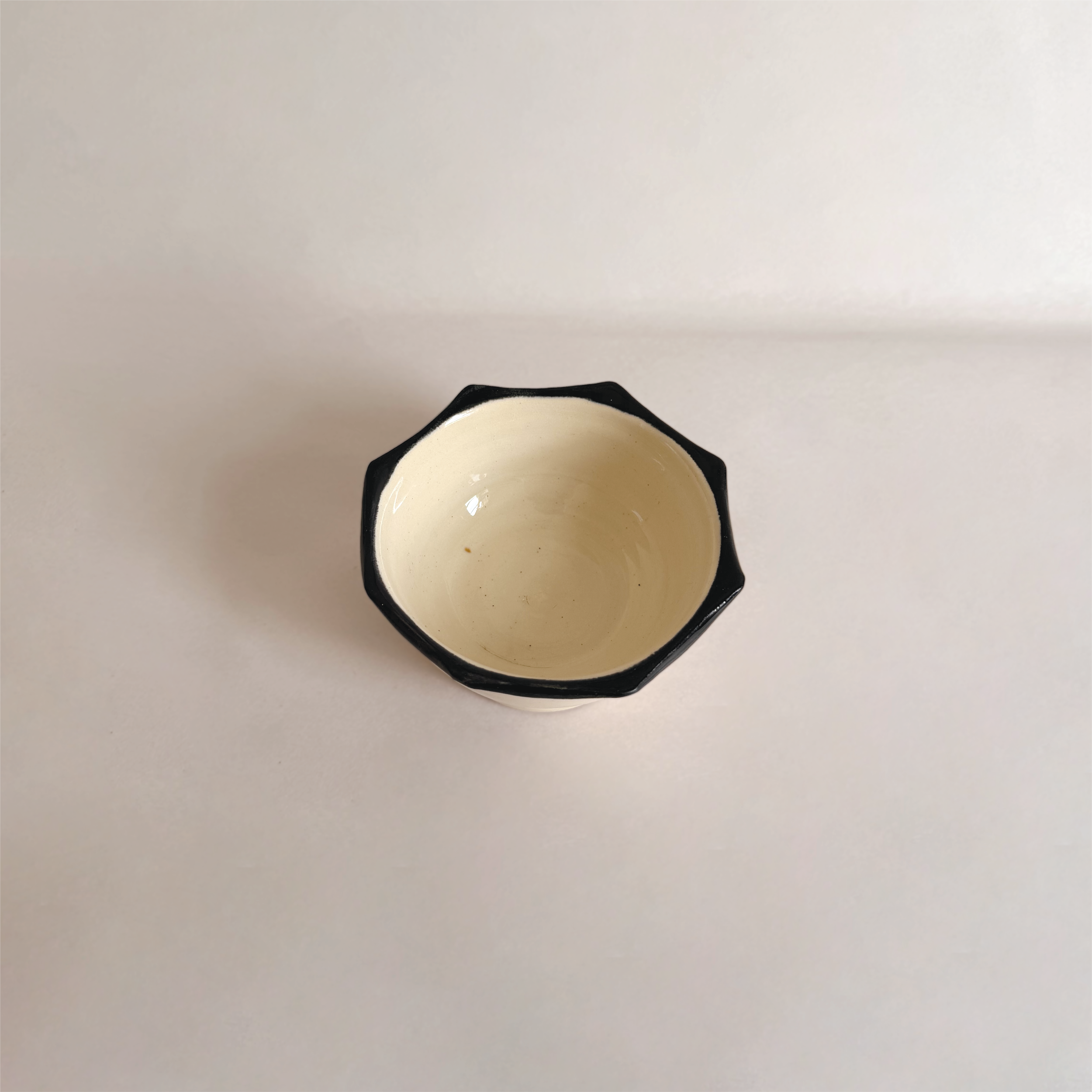 Top-down view of a white ceramic cup with a black scalloped rim, sitting on a white surface.