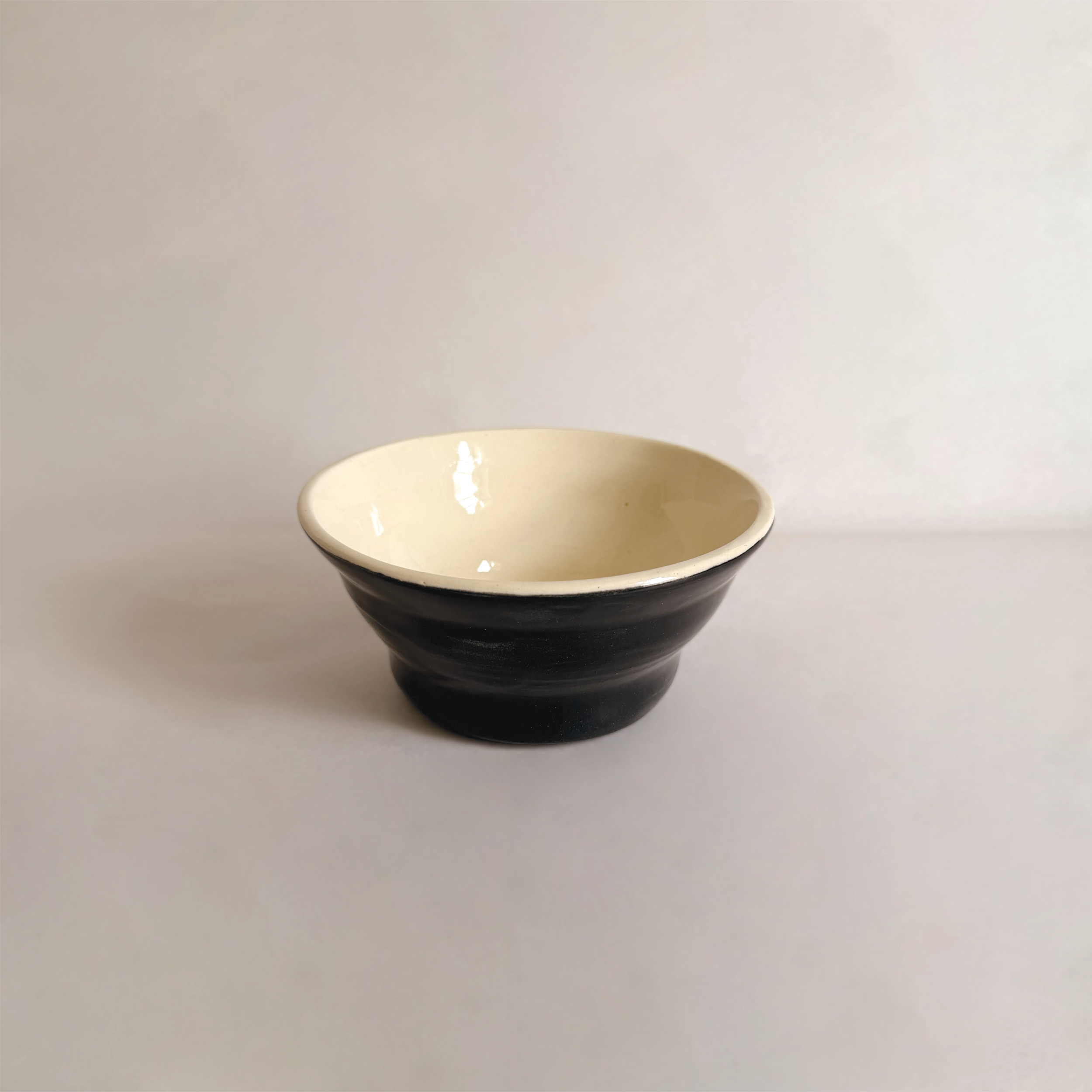 A small black and white ceramic bowl on a white surface against a plain background.