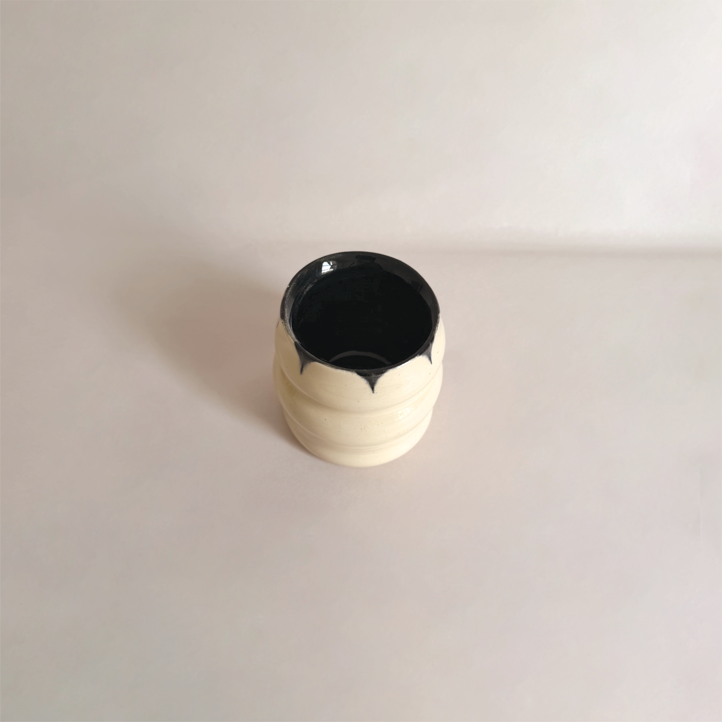 A small, round ceramic vase with a black interior and a white exterior, placed on a white surface.