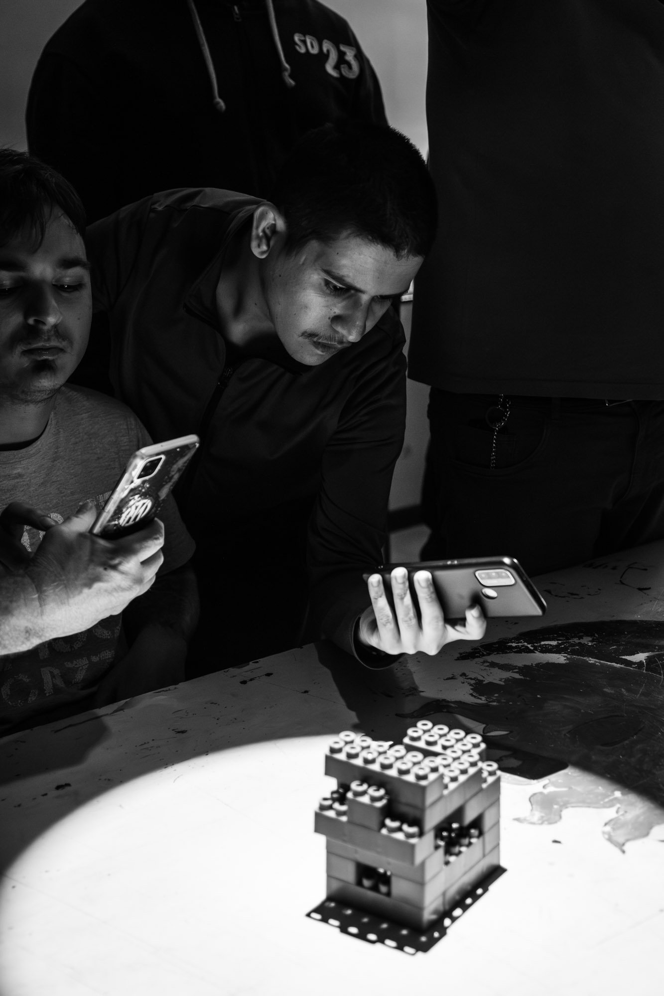 Gruppo di persone che fotografano una torre costruita con le costruzioni, in un ambiente interno.