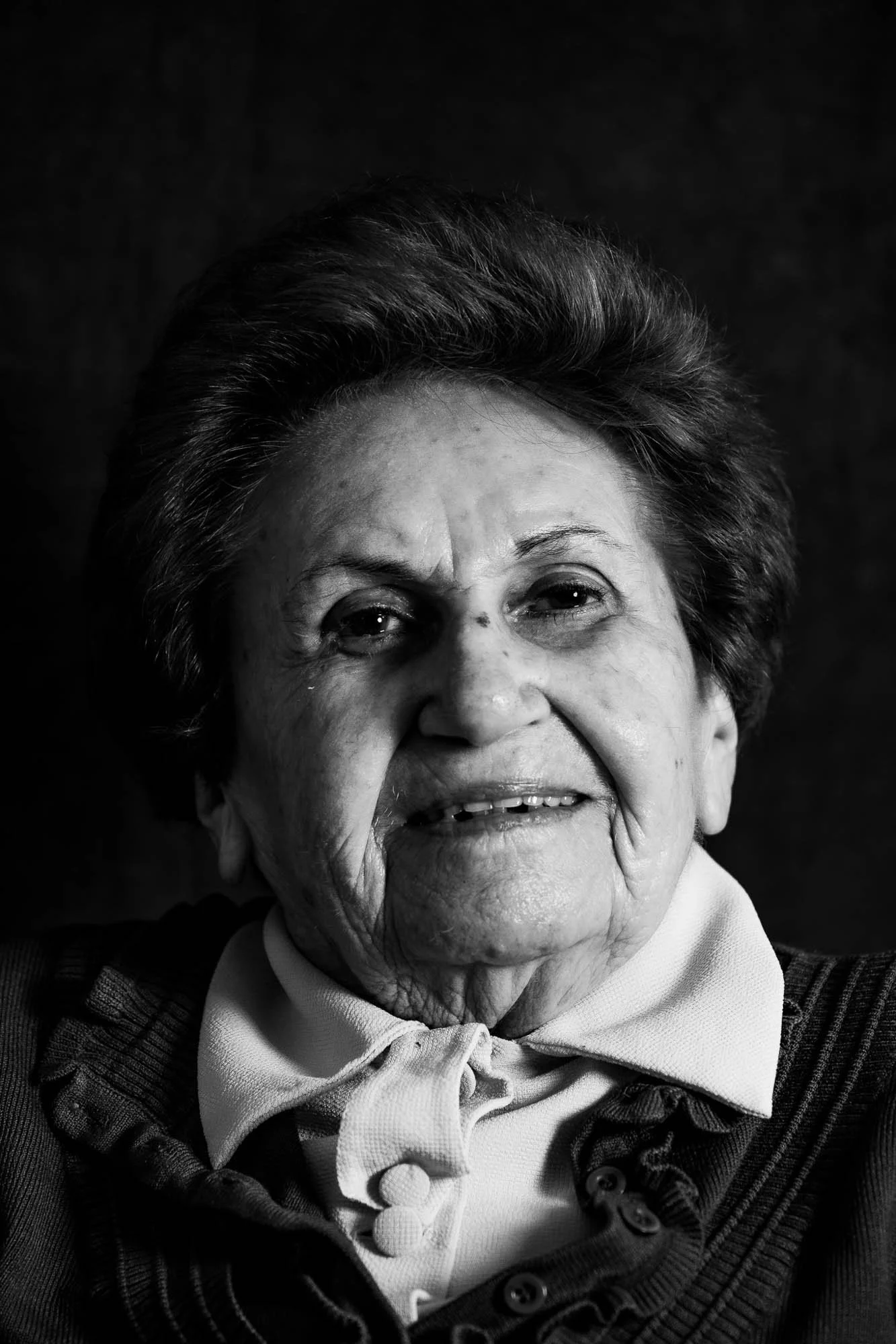 Ritratto in bianco e nero di una donna anziana sorridente con capelli corti e vestito scuro con una sciarpa bianca