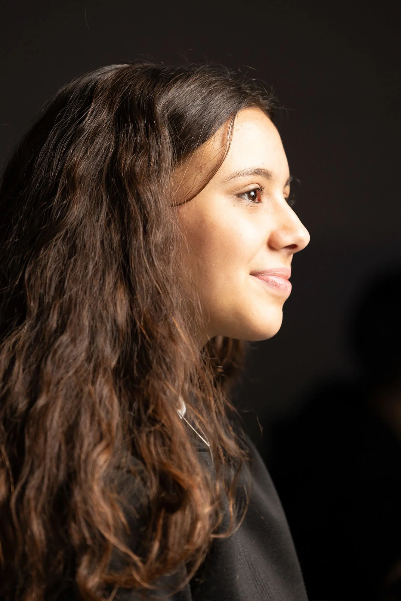 Ritratto di una ragazza con capello riccio castano chiaro, sorriso leggero, sfondo nero.