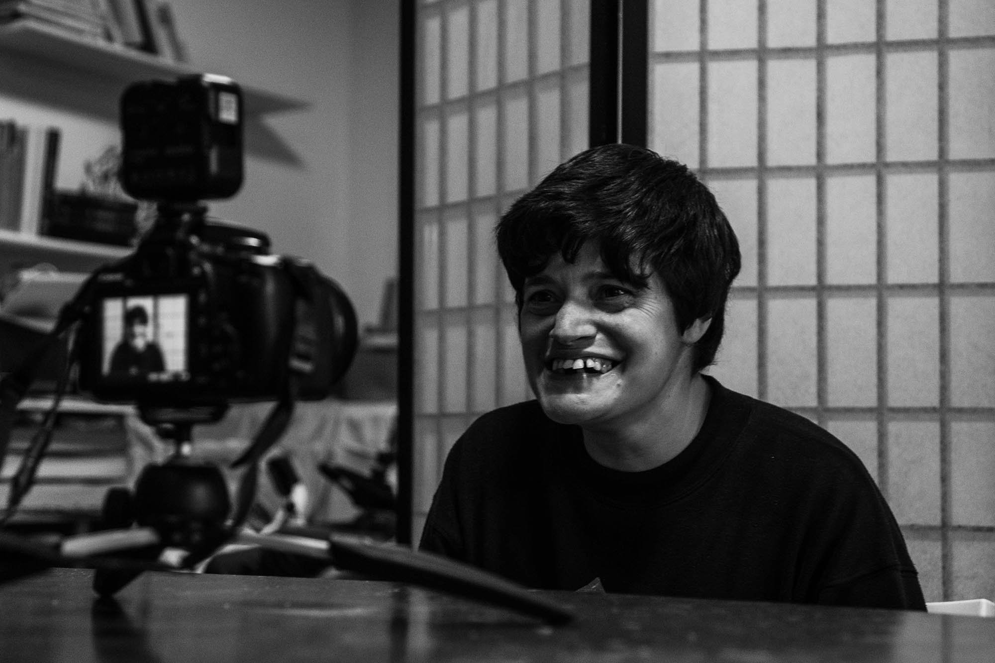 Ritratto di una donna sorridente con capelli corti, visibile attraverso una fotocamera.