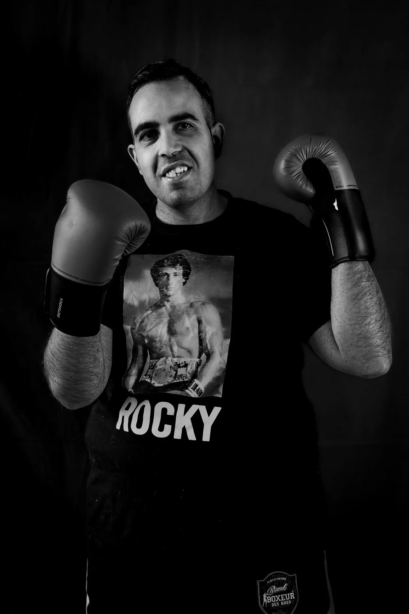 Uomo con guantoni da boxe in posa frontale, indossa una maglietta con l'immagine di Rocky Balboa.