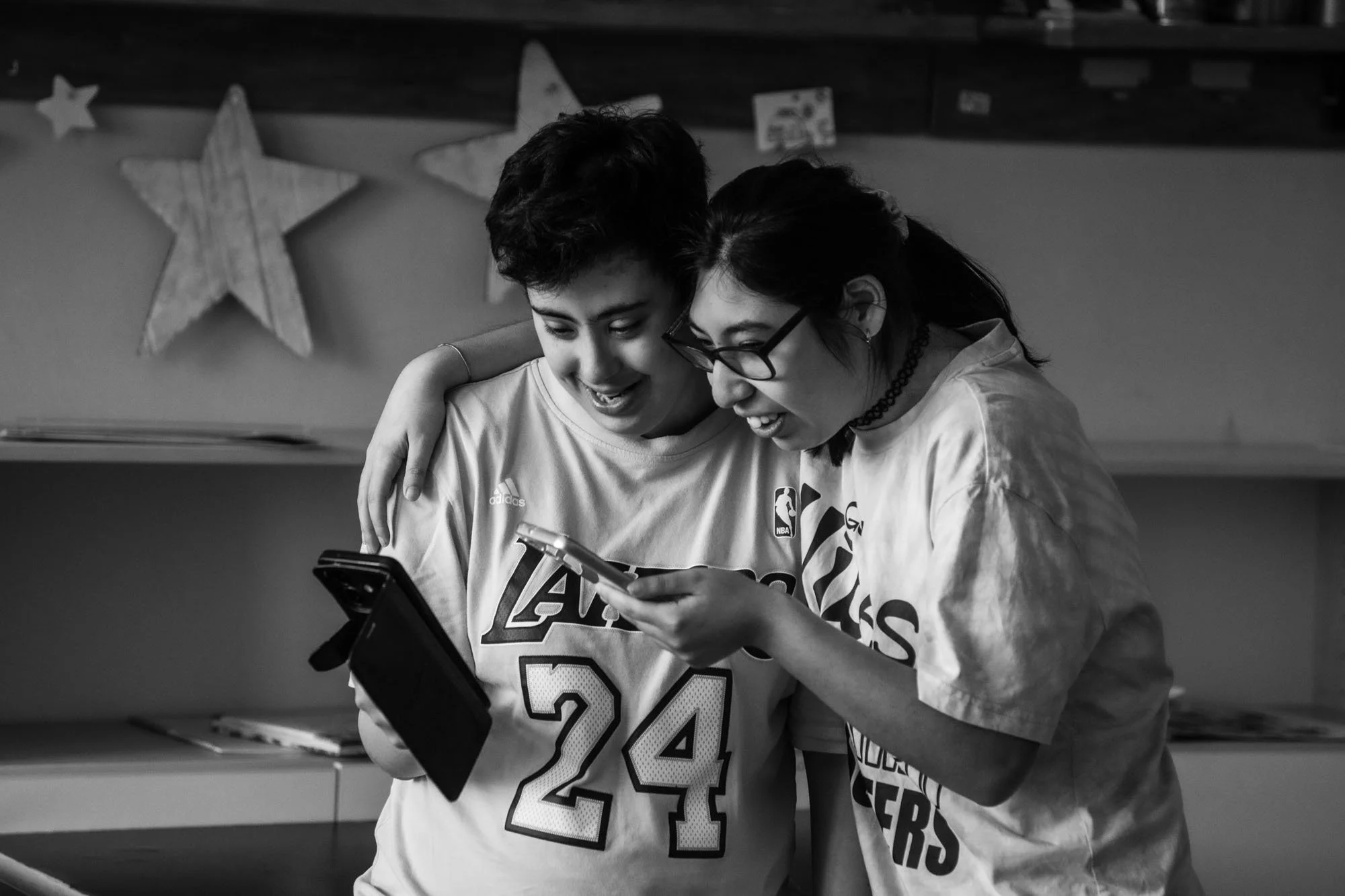 Due giovani donne sorridenti guardano uno smartphone, con lo sfondo decorato da stelle di carta.