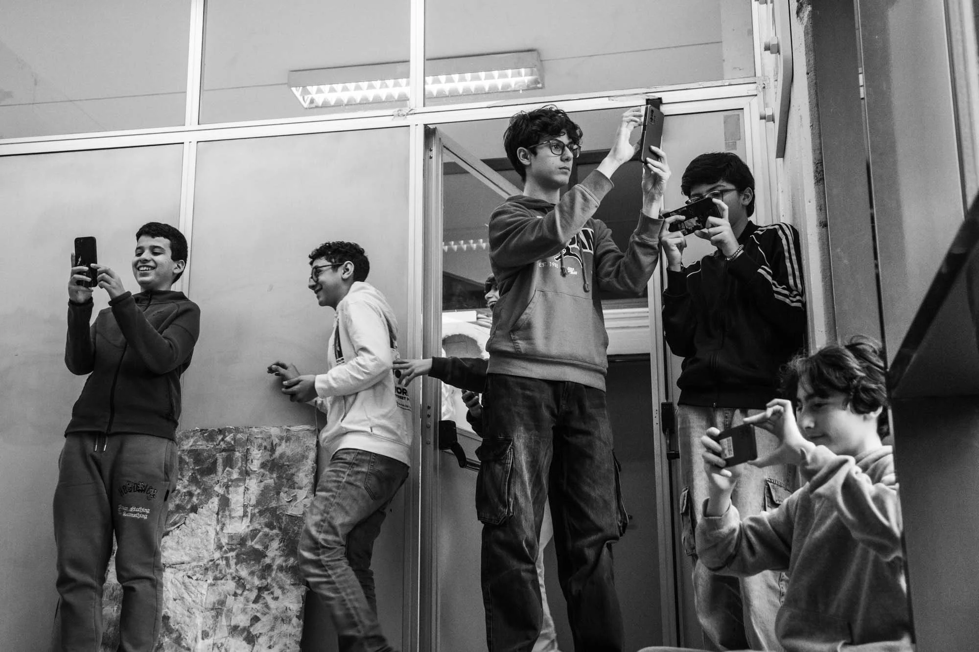 Gruppo di giovani ragazzi che scattano foto con i loro smartphone in un ambiente interno, alcuni sorridenti e intenti a immortalare il momento.