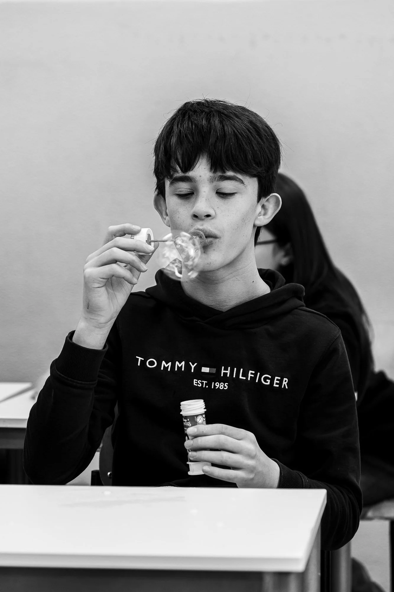 Ragazzo che soffia bolle di sapone in un ambiente interno, indossa una felpa Tommy Hilfiger.