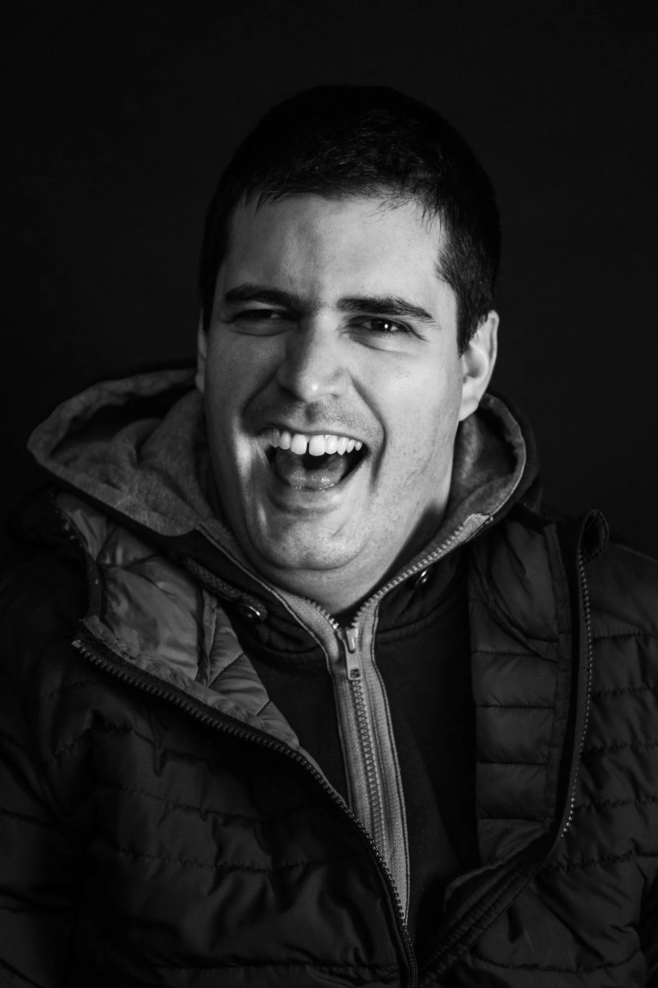 Foto di un uomo sorridente che indossa una giacca zip-up, con sfondo nero.