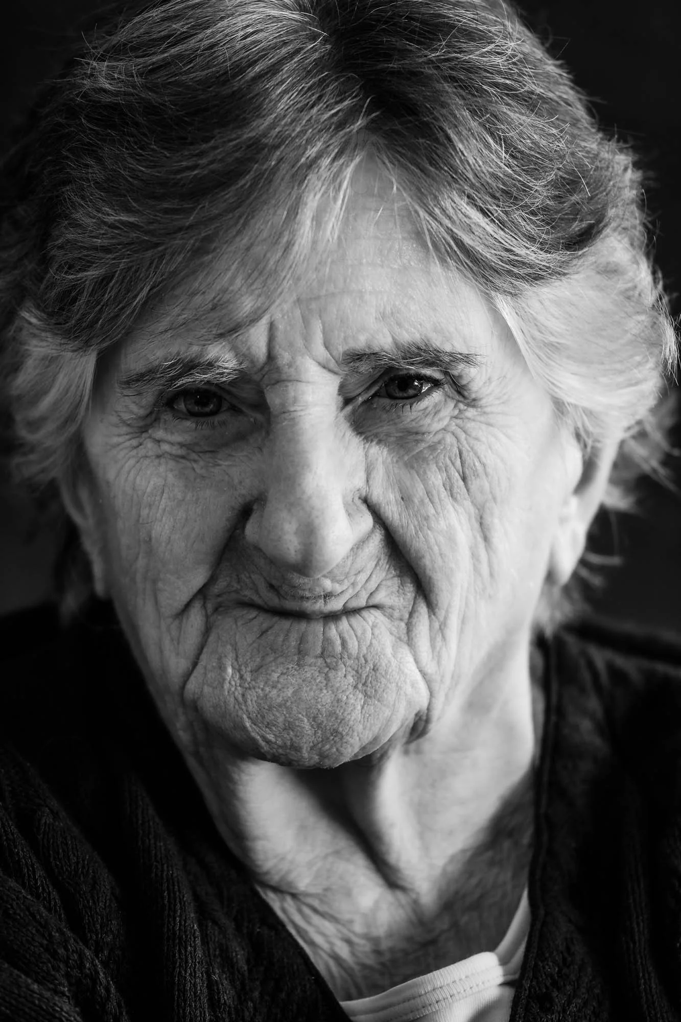 Ritratto di una donna anziana con capelli grigi e pelle rugosa, viso serio, in bianco e nero.