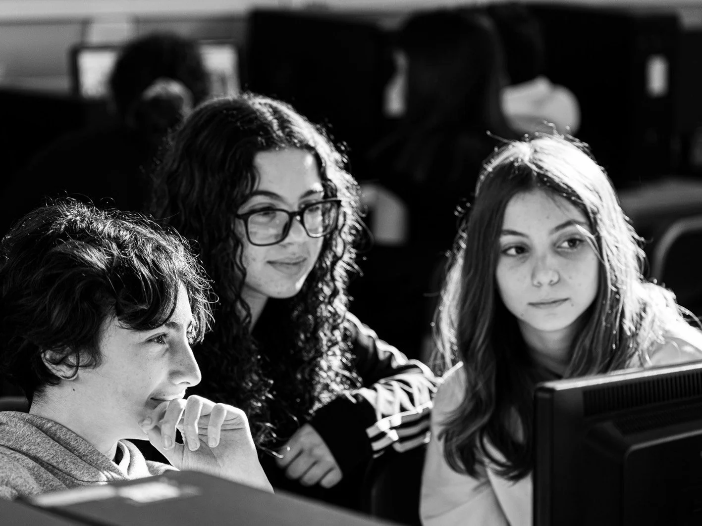 Un ragazzo e due ragazze seduti davanti a un computer, impegnati in un'attività di gruppo al computer, in un'aula di informatica.
