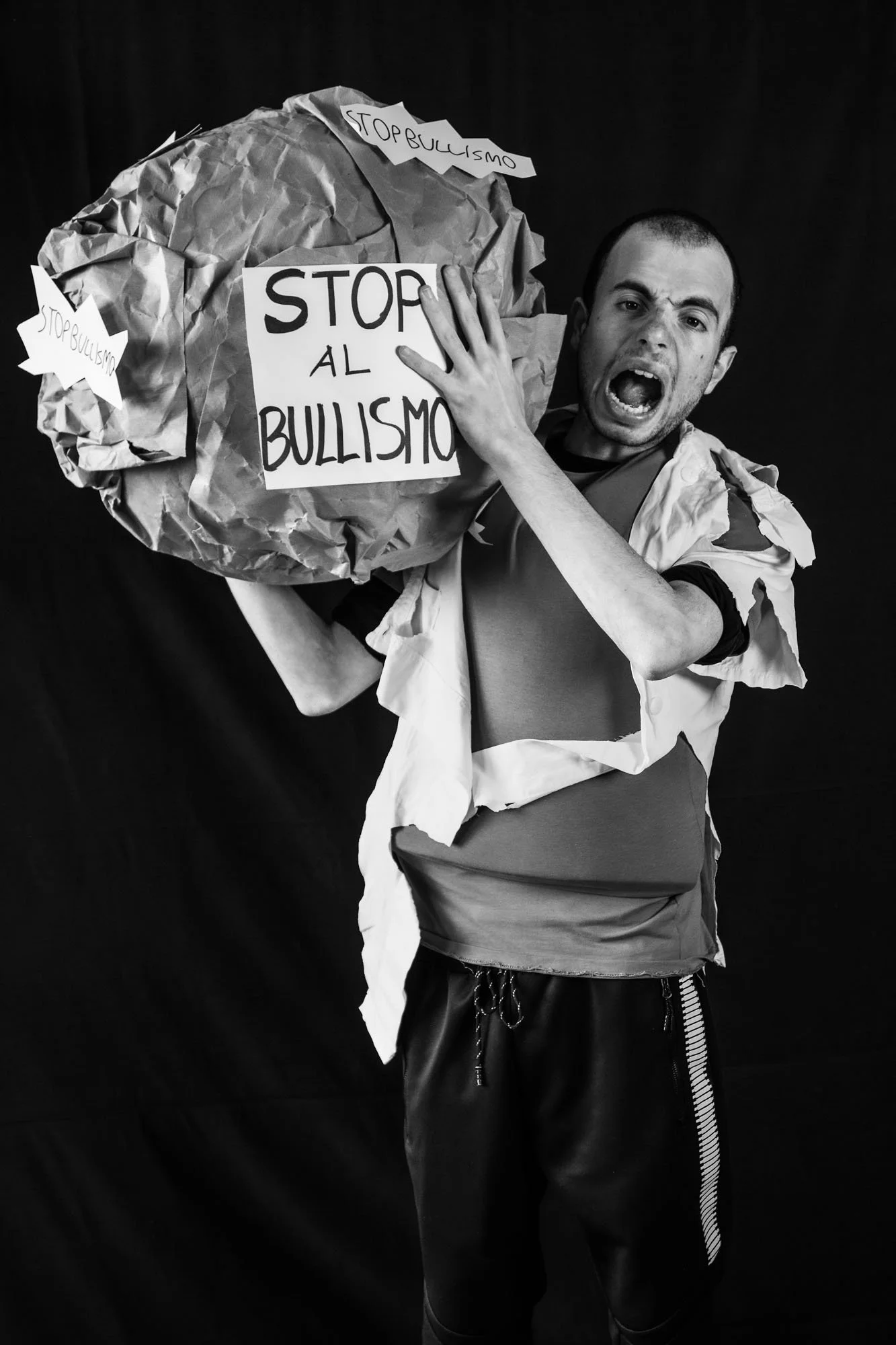 Un giovane uomo che sembra urlare mentre tiene un tumulo di carta con un cartello che dice 'STOP AL BULLISMO'.