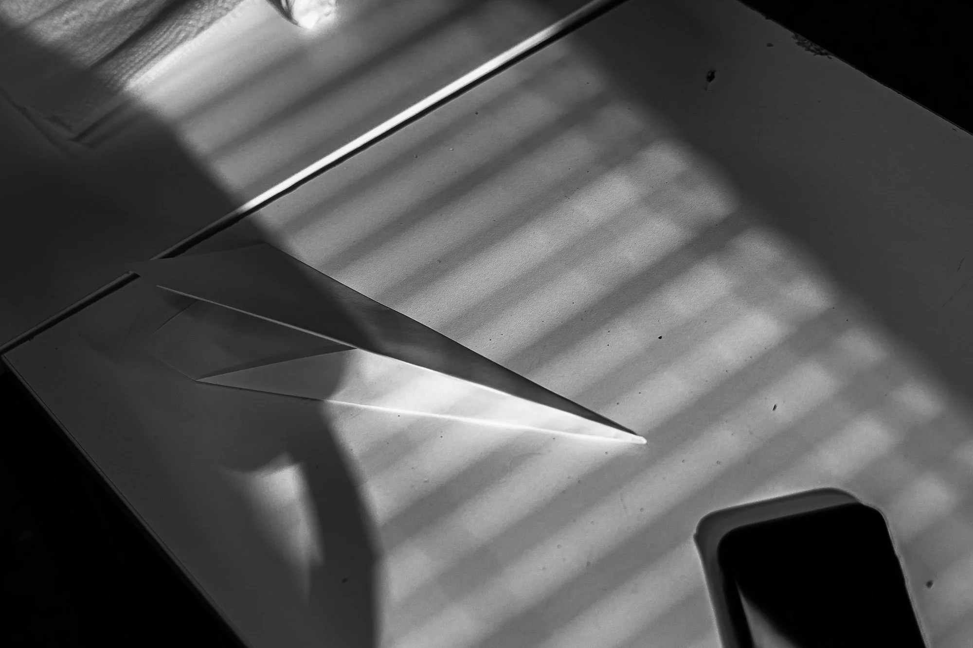 Foto in bianco e nero di un aeroplano di carta con un gioco di luci e ombre sul tavolo.