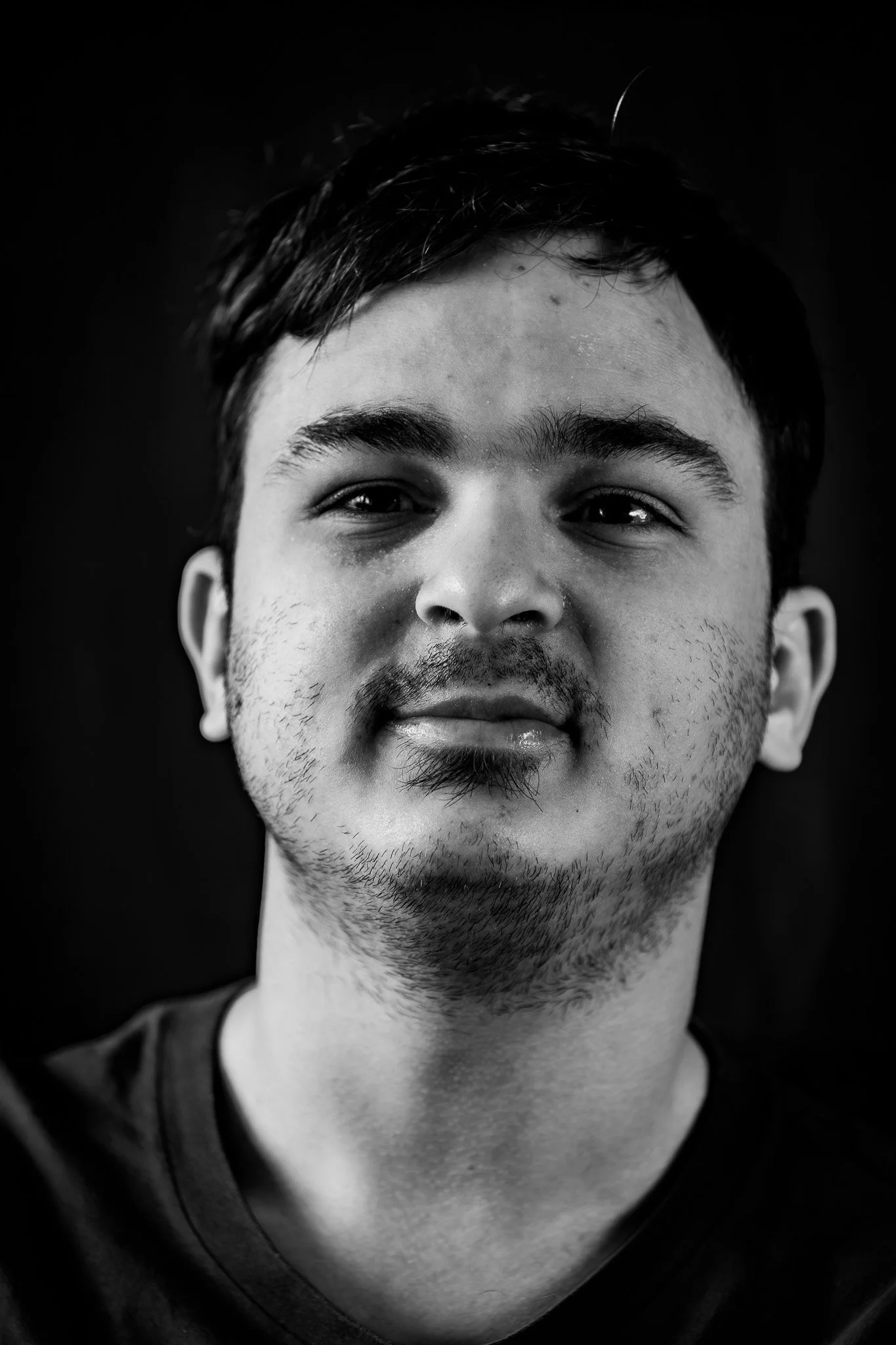 Ragazzo con capelli corti, barba leggera e sorriso, in primo piano in una fotografia in bianco e nero.