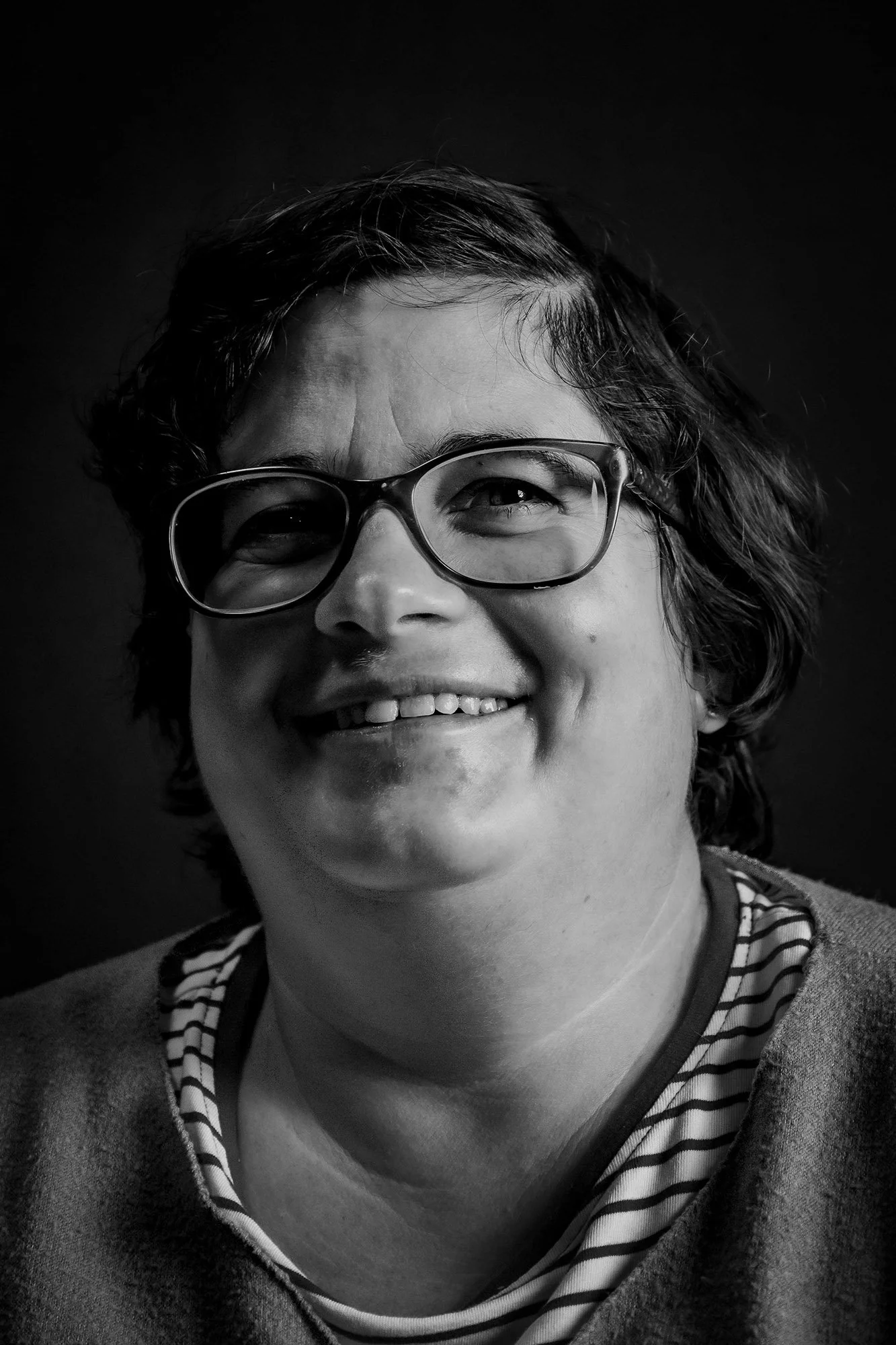 Ritratto in bianco e nero di una donna con capelli ricci, occhiali e sorriso.