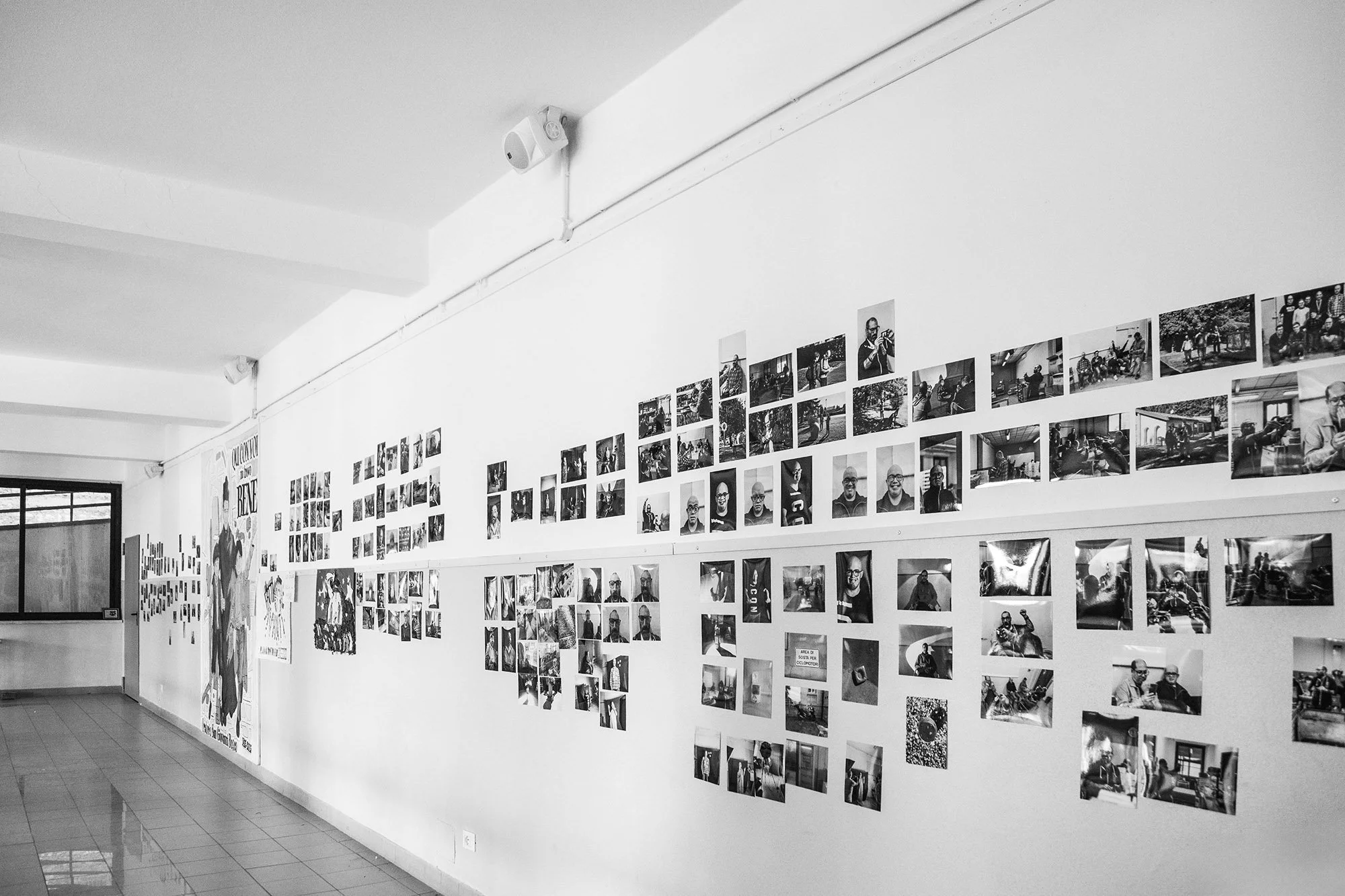 Mostra fotografica su una parete di una galleria, con moltissime foto in bianco e nero di persone e scene di vita quotidiana.