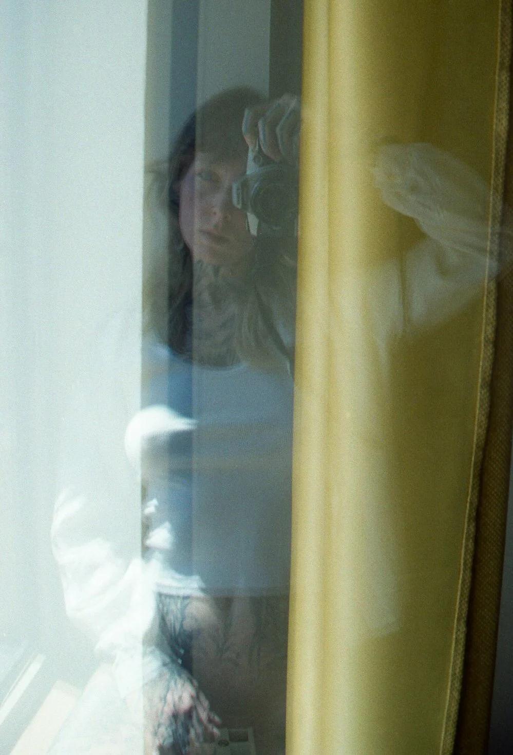 Reflet d'une femme prenant une photo avec un appareil photo, vue à travers une vitre ou une surface réfléchissante, avec un outline jaune en arrière-plan.