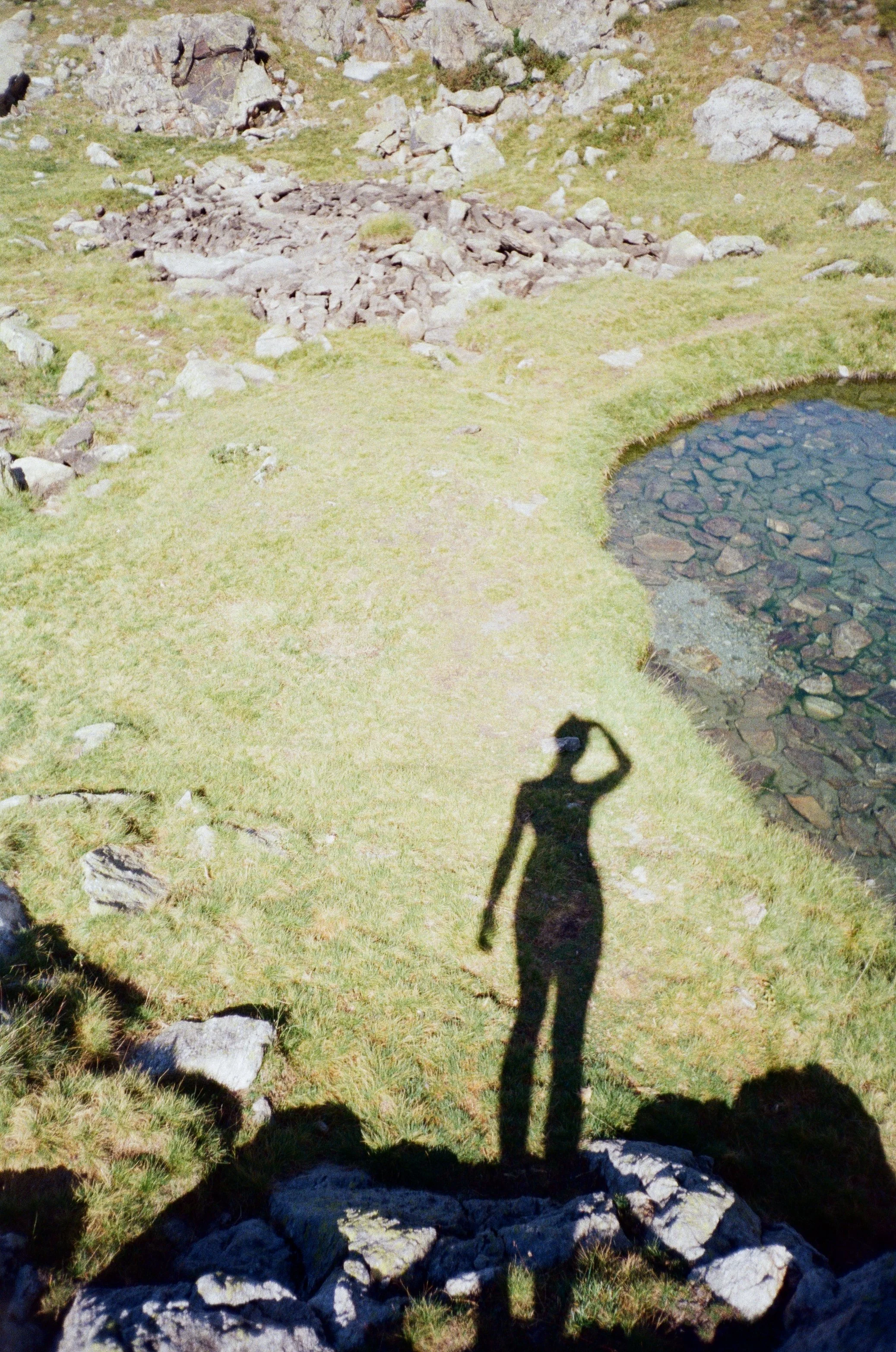 Ombre d'une femme prenant une photo dans un paysage de nature avec un étang et des rochers, en plein soleil.