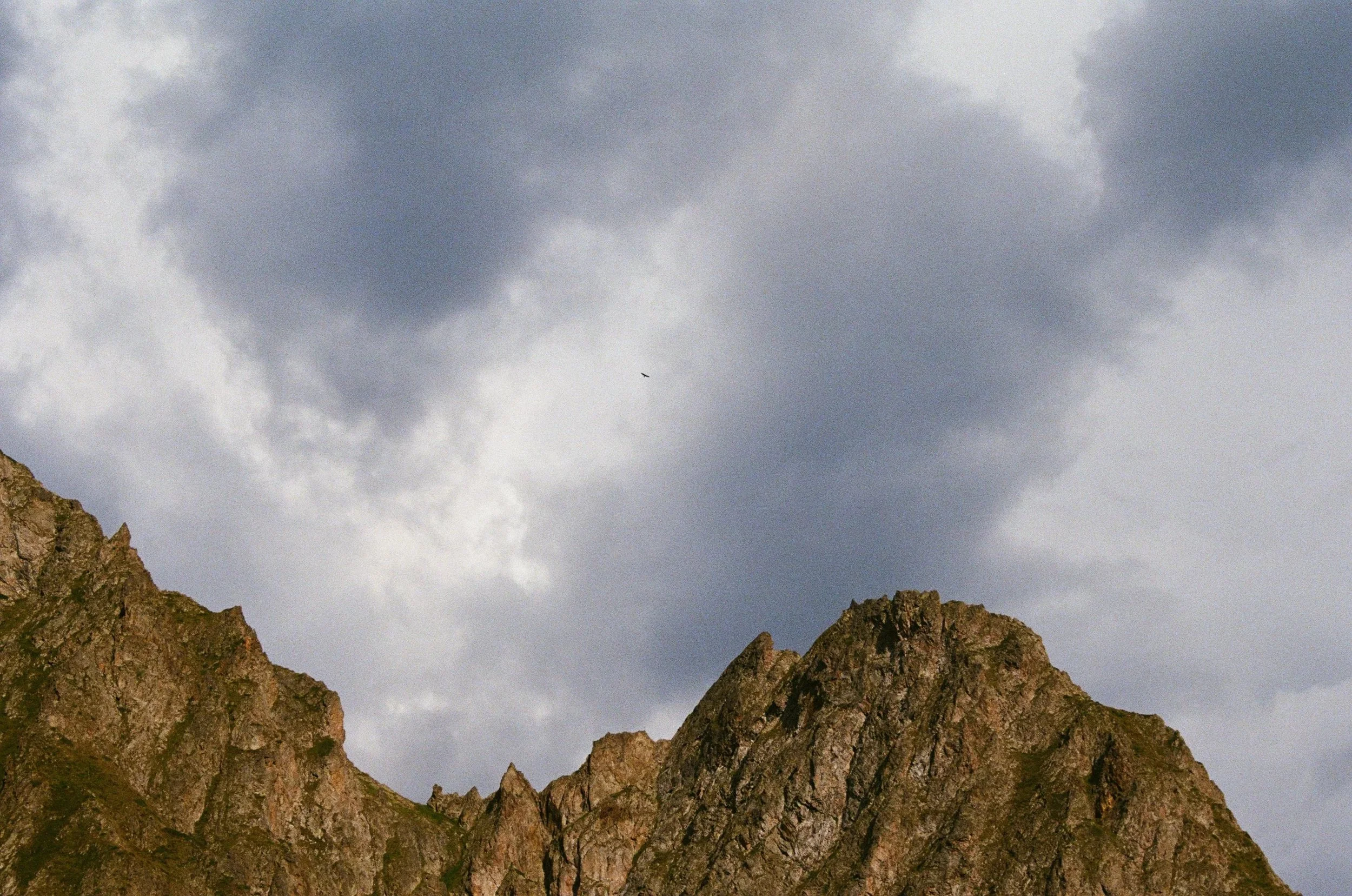 Montagnes rocheuses sous un ciel nuageux avec un oiseau volant en haut