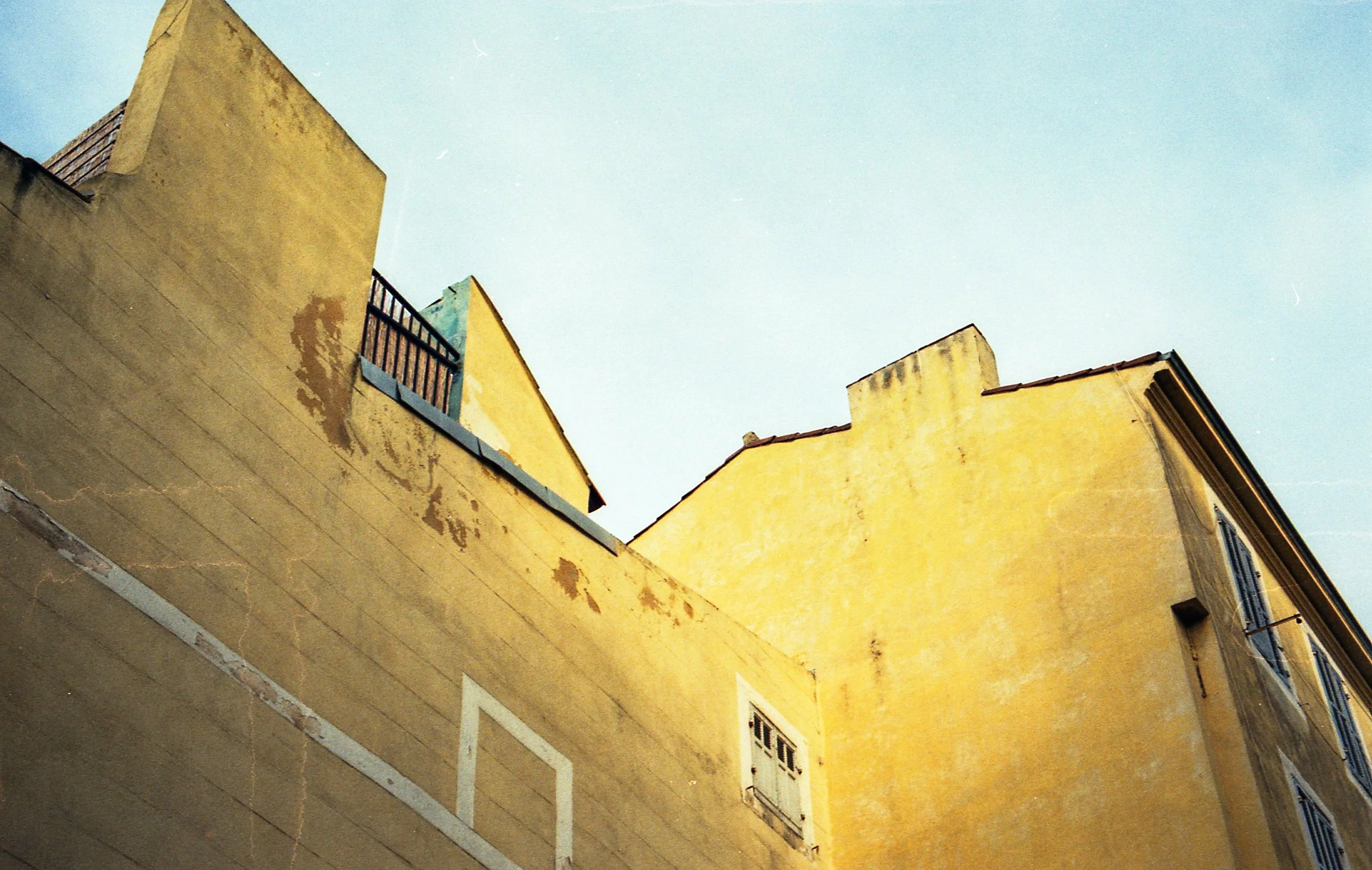 Photo de bâtiments jaunes avec des fenêtres, vu de bas vers le haut, avec un ciel clair en arrière-plan.
