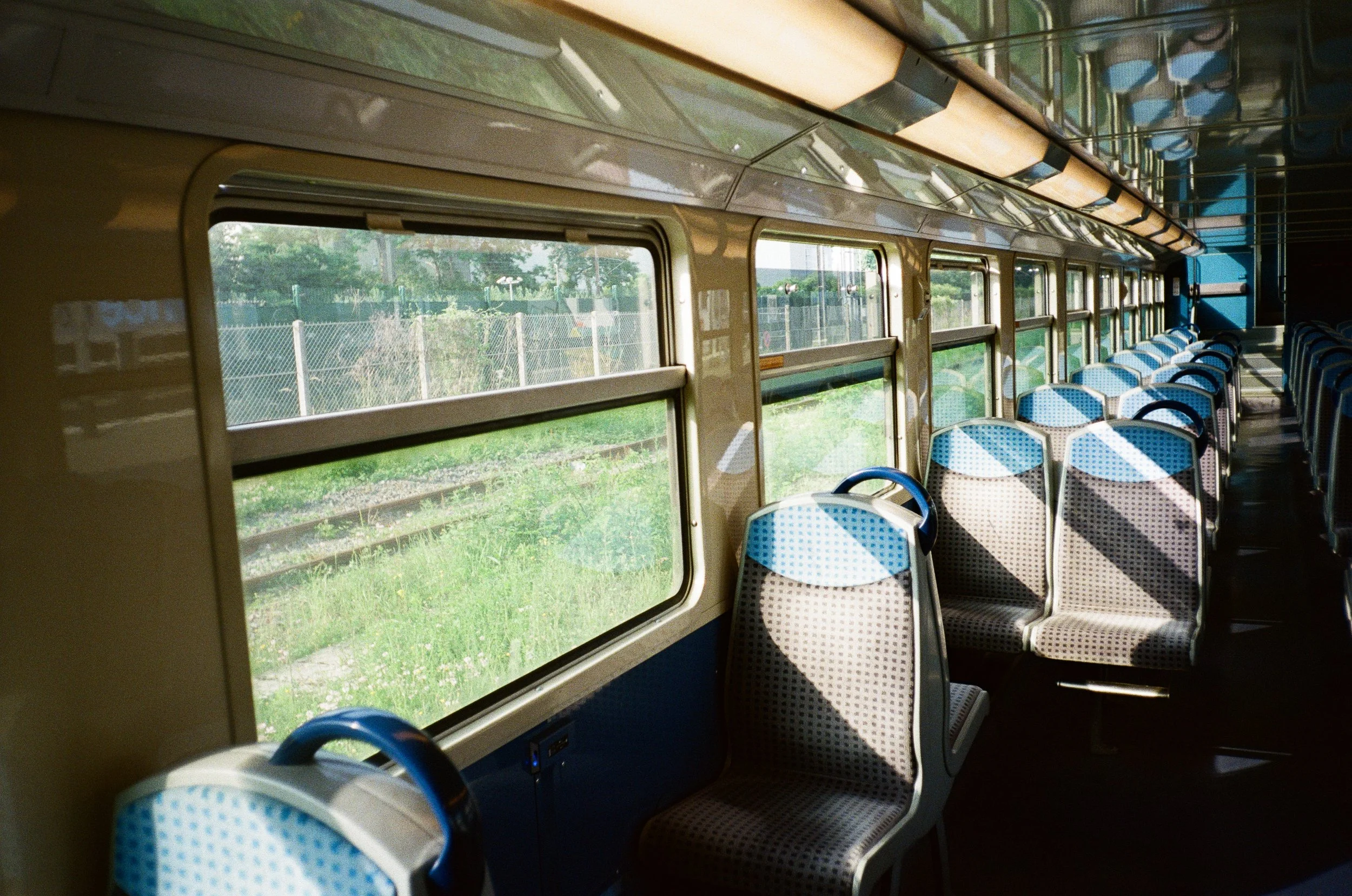 Intérieur d'un train avec des sièges en tissu à motif bleu, des fenêtres laissant voir un paysage verdoyant extérieur, et un éclairage tamisé.