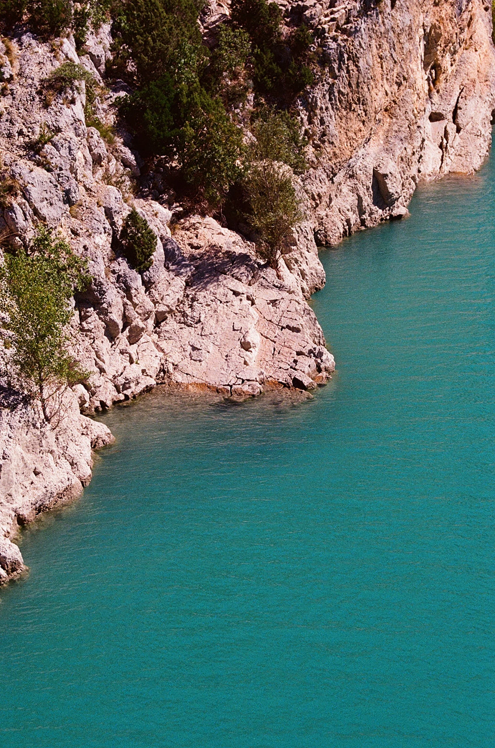 Côte rocheuse avec de la végétation, bordée d'une eau turquoise calme.