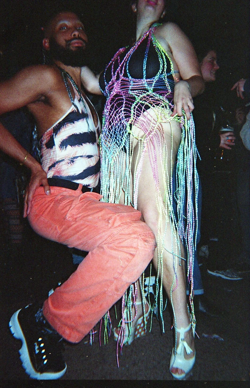 Deux personnes posent lors d'un événement, l'une portant un vêtement en fil lumineux et l'autre en pantalon orange et haut à motifs zebra.