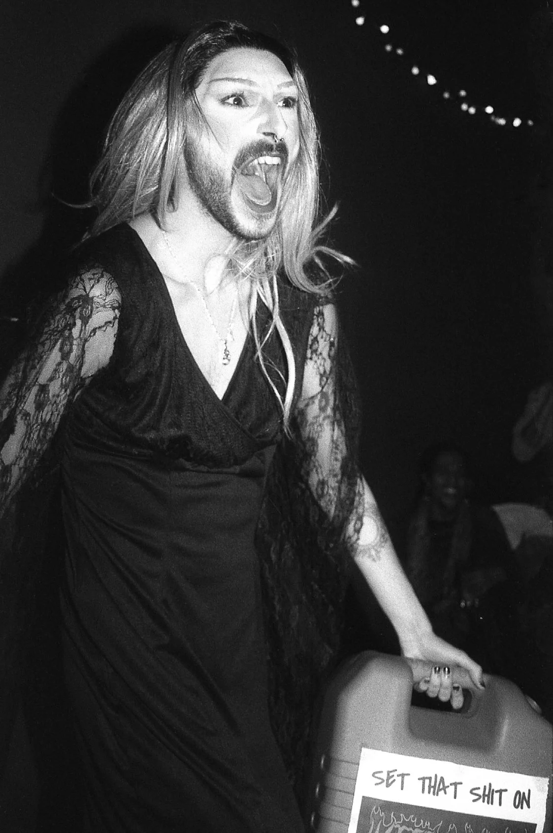 Une personne en train de crier ou chanter avec une expression intense, portant une robe noire en dentelle avec manchettes en dentelle.