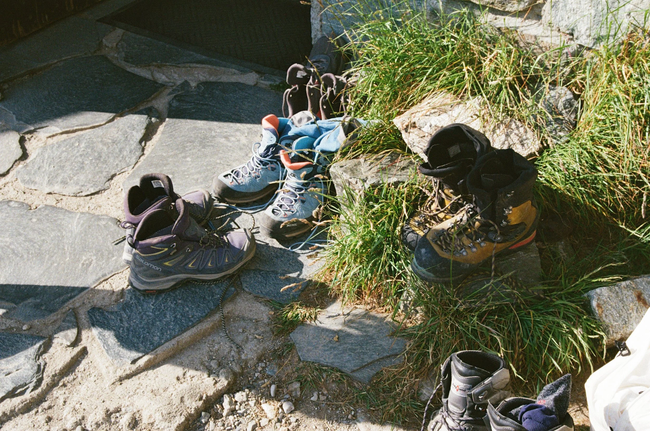 Chaussures d'escalade et de randonnée posées sur un sol rocheux et herbeux.