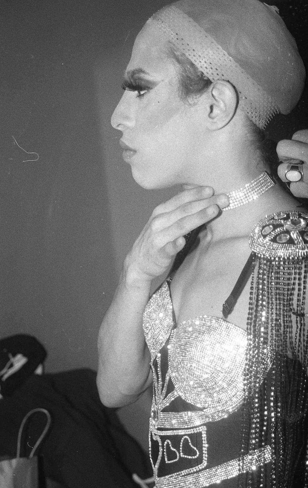 Portrait en noir et blanc d'une femme portant des bijoux en strass, un vêtement orné de motifs brillants, semblable à une tenue de scène ou de spectacle.