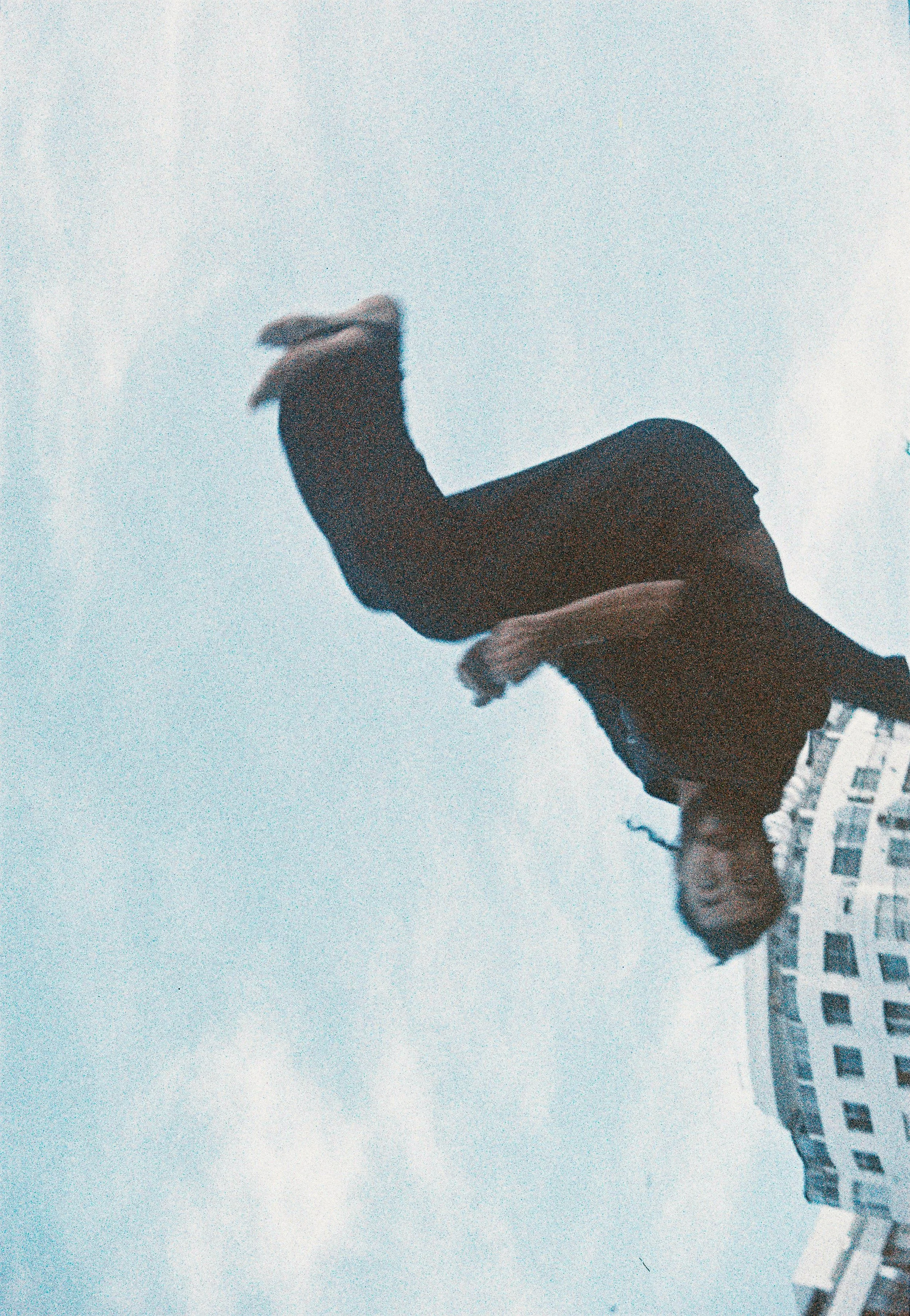 Une femme blonde portant un manteau noir et une paire de lunettes, toute souriante, pose devant un bâtiment résidentiel moderne.