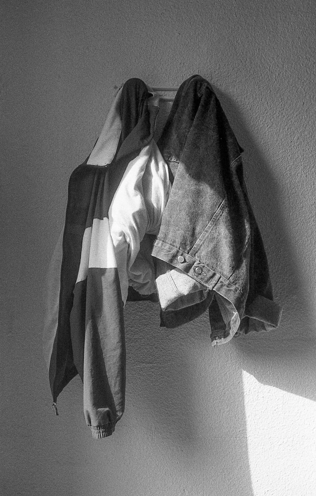 Vêtements suspendus dont une veste en denim et un foulard ou une écharpe, accrochés à un crochet sur un mur.