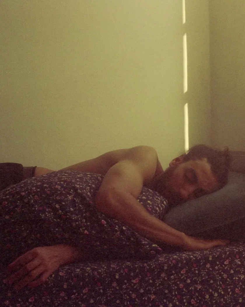 Une personne allongée sur un lit, se reposant dans une pièce doucement éclairée par la lumière naturelle filtrant à travers des volets.