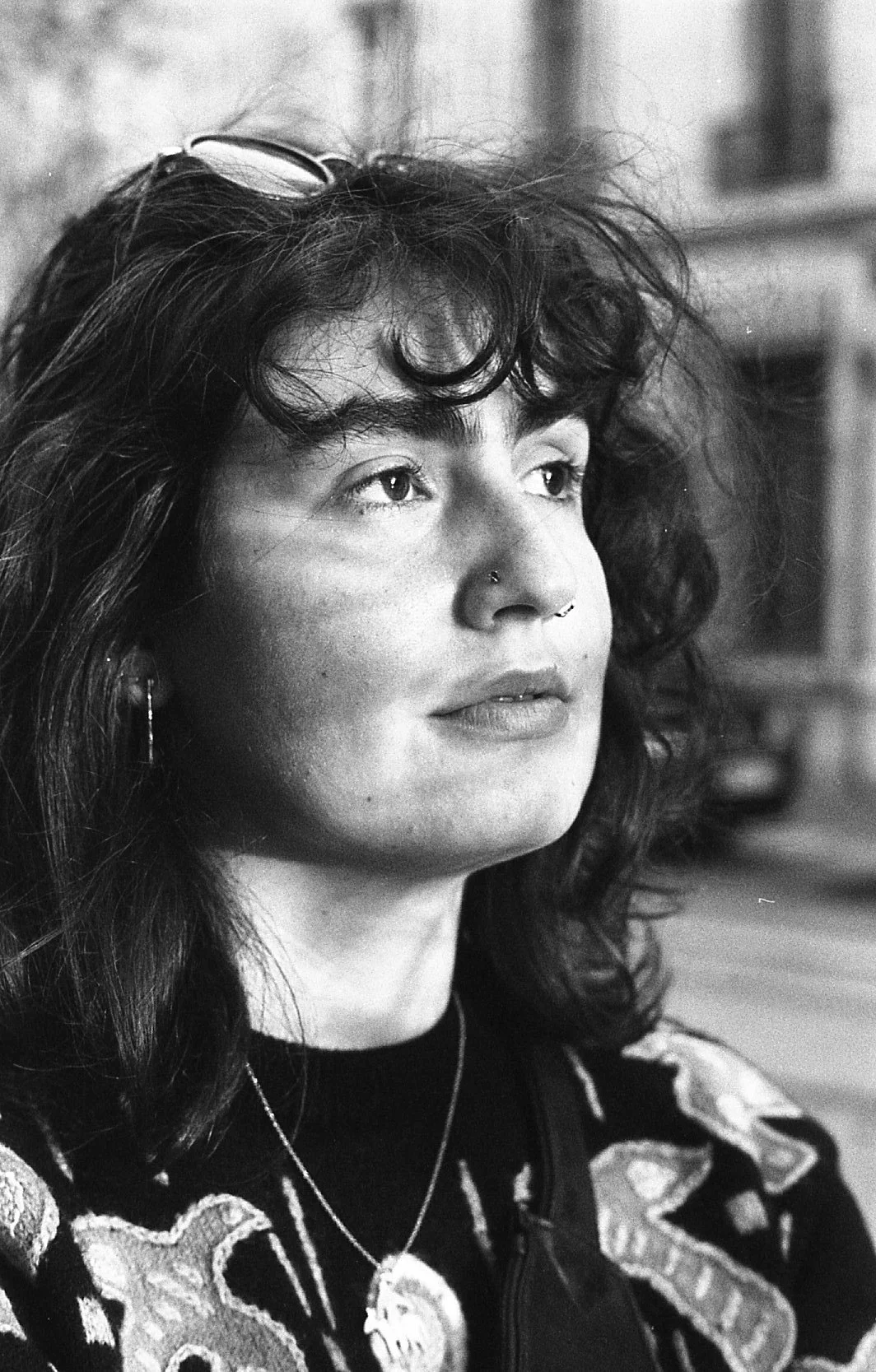 Portrait en noir et blanc d'une femme avec des cheveux bouclés, portant des piercings au nez et des boucles d'oreilles, regardant vers la gauche.