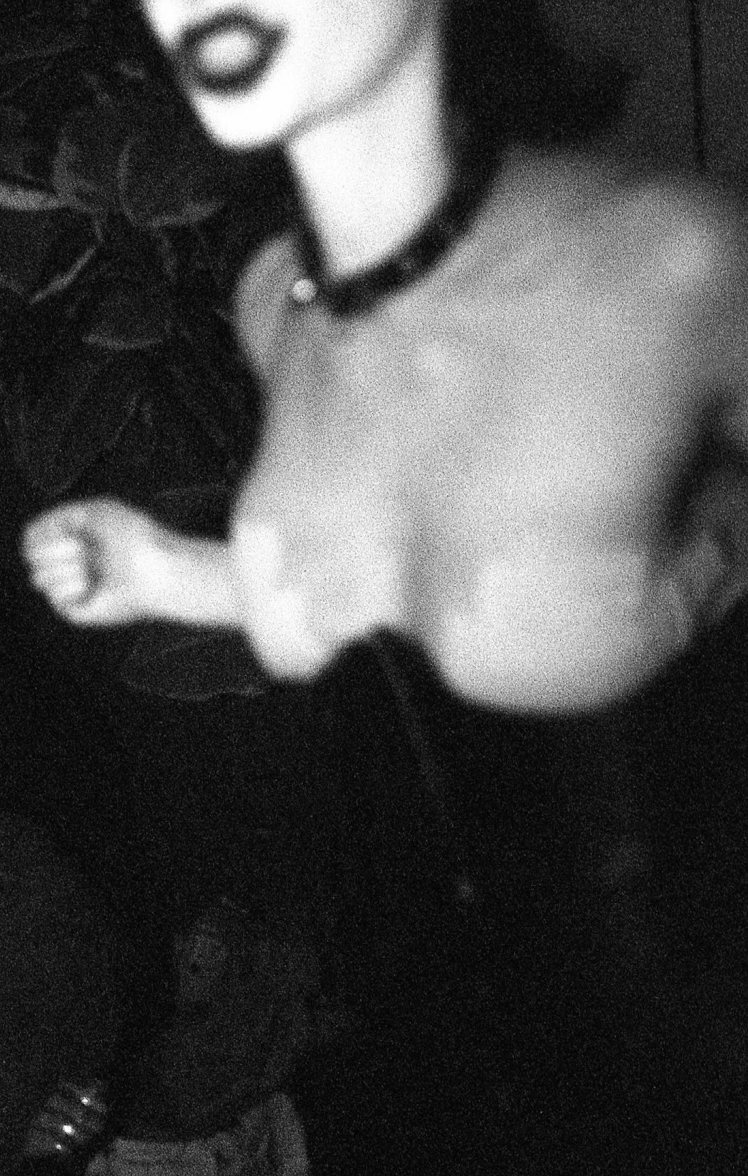 Une personne porte des lunettes de soleil, un collier, un haut décolleté, et un bracelet, avec un fond sombre.