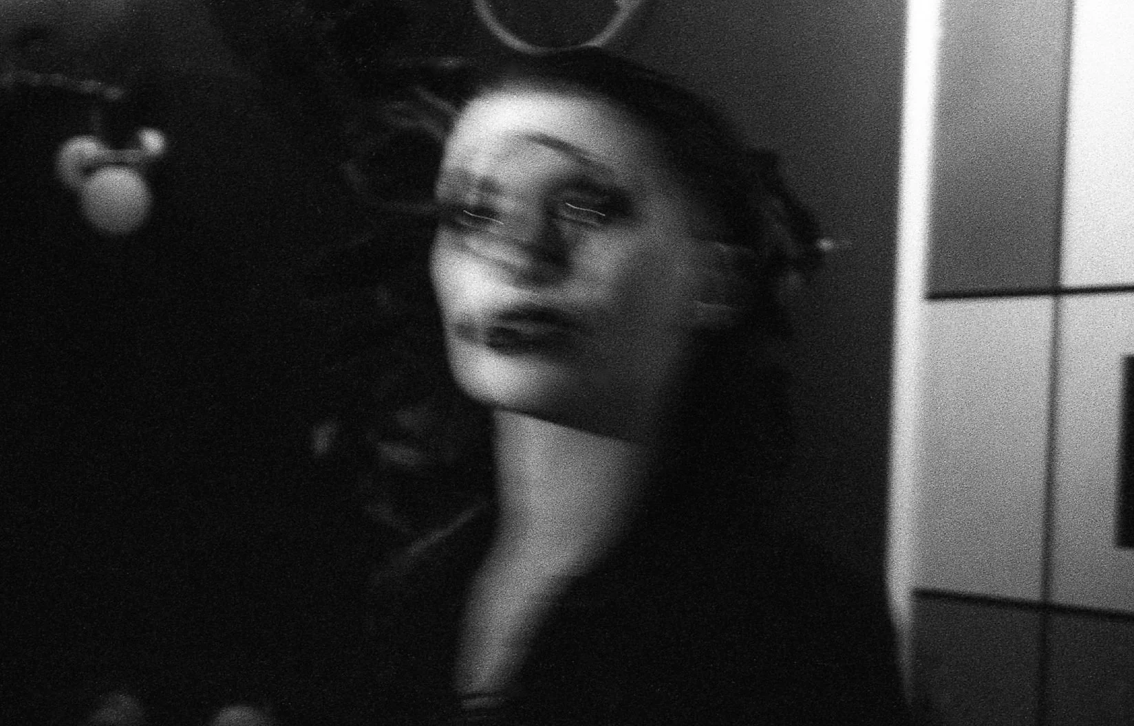 Une photo en noir et blanc d'une femme avec un maquillage sombre et des cheveux bouclés, posant contre un mur.