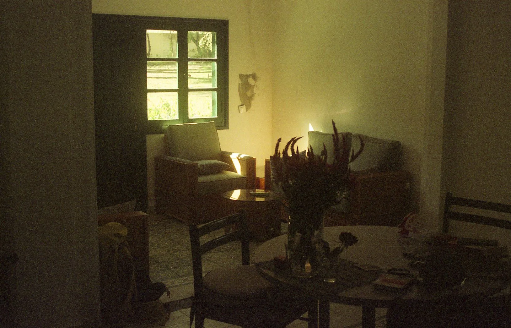 Intérieur sombre d'une pièce avec un fauteuil et une table, éclairée par la lumière filtrant à travers une fenêtre.