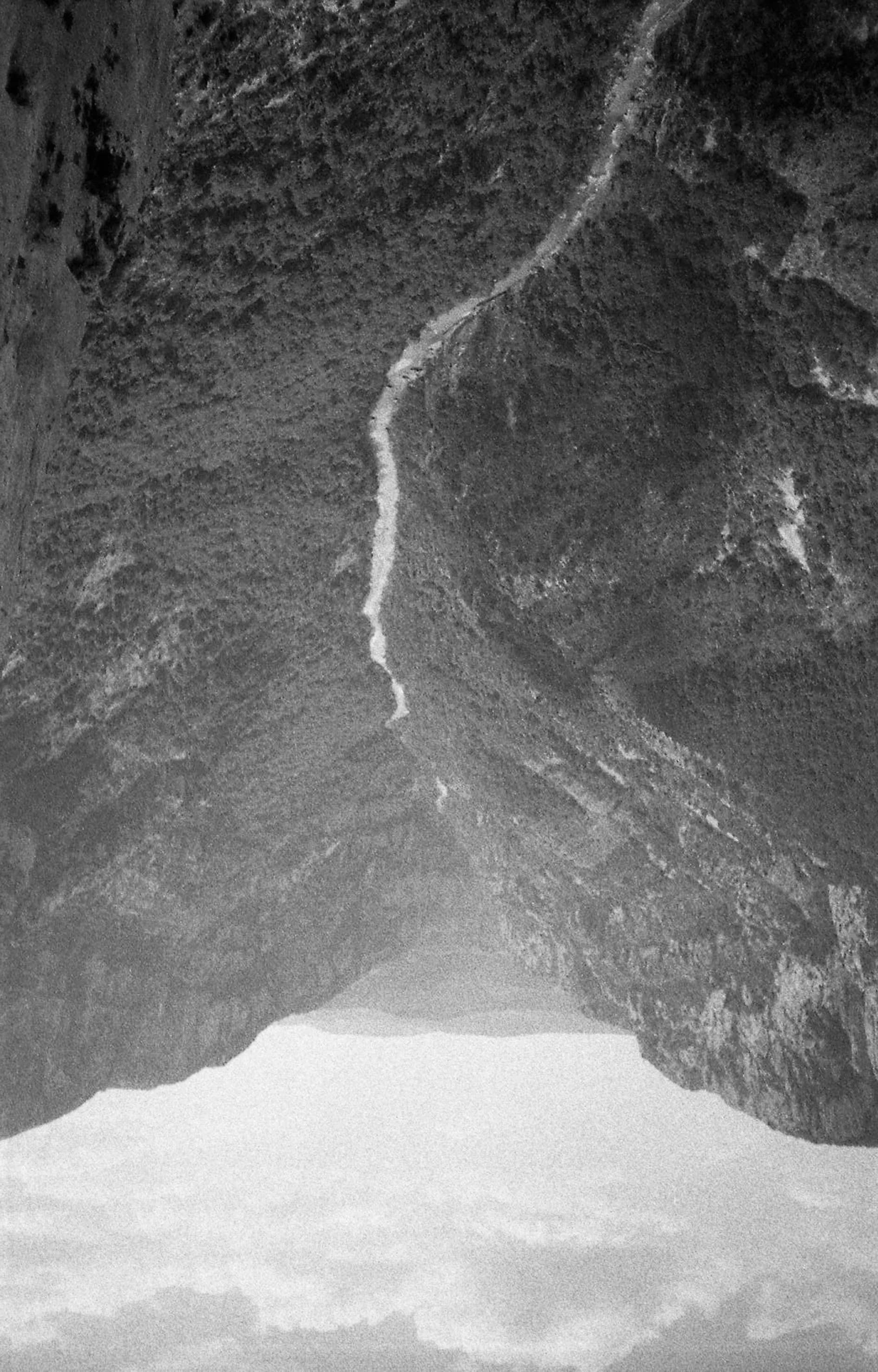 Vallée rocheuse vue en contre-plongée, avec des falaises escarpées et un canyon profond, en noir et blanc.