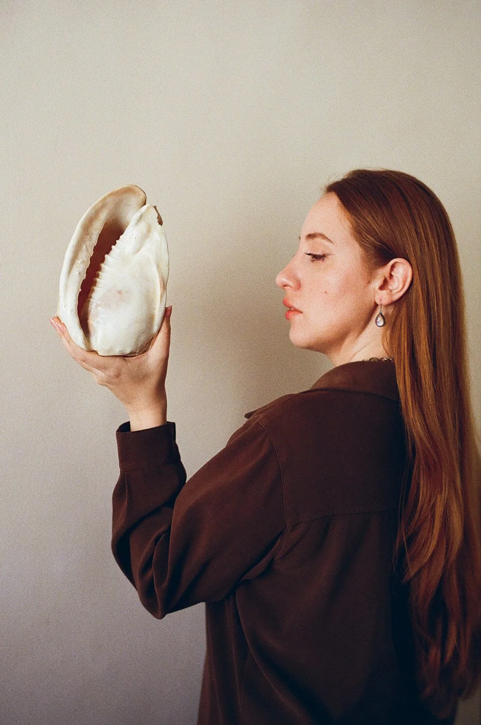 Femme aux cheveux roux regardant une grande coquille d'ormeau qu'elle tient en main.