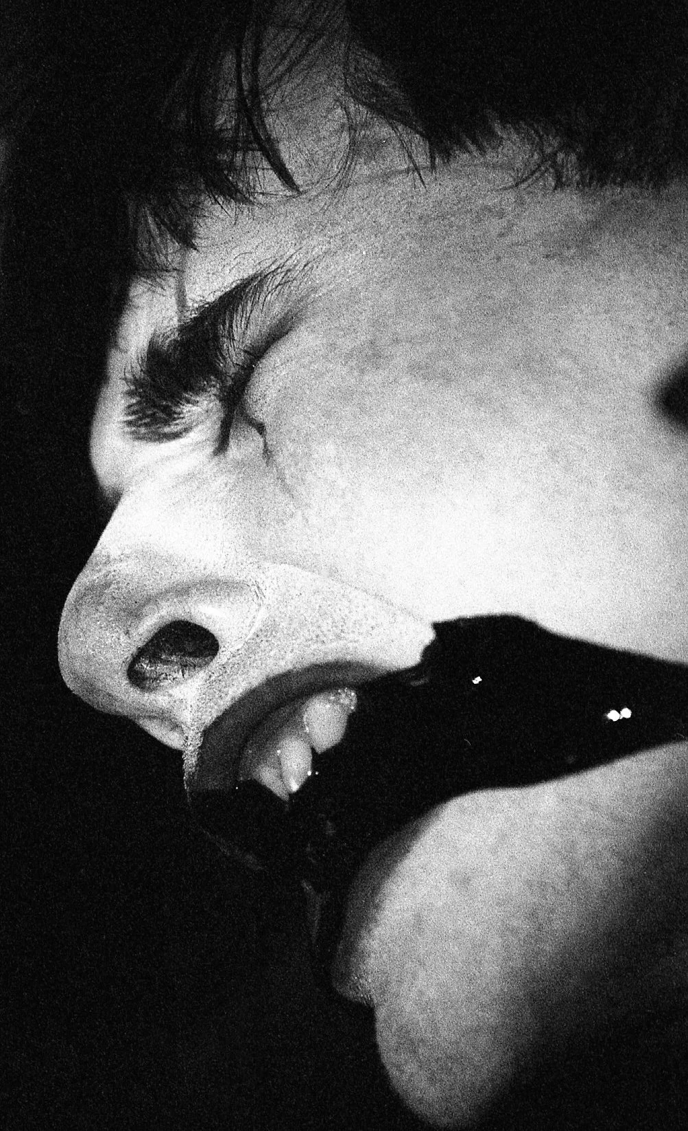 Close-up en noir et blanc d'un visage humain avec une expression de colère ou de douleur, yeux fermés, nez et bouche visibles.