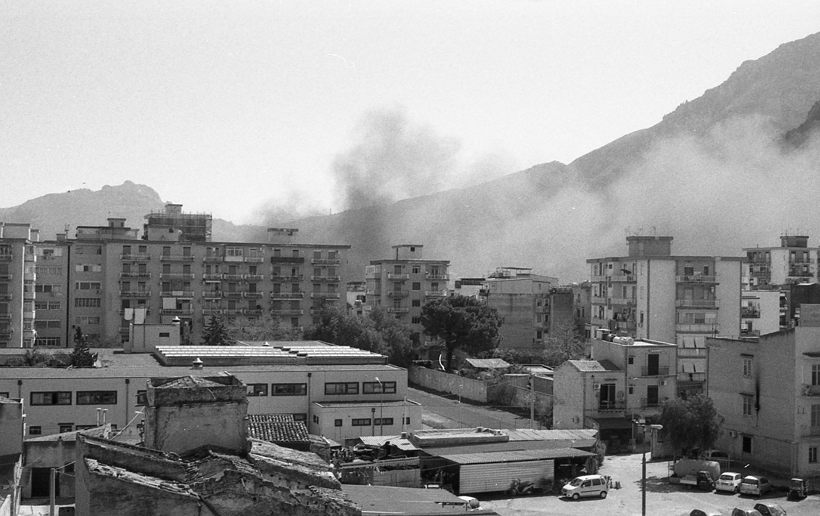 Un ensemble de bâtiments résidentiels avec des montagnes en arrière-plan, où l'on peut voir de la fumée s'élevant de la montagne.