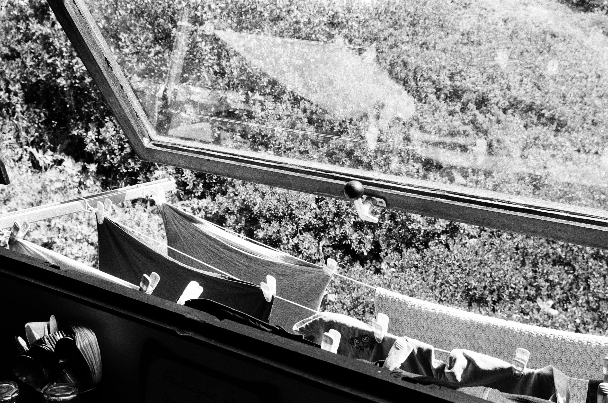 Vue depuis une fenêtre ouverte sur des vêtements suspendus à une corde à linge dans un jardin with foliage